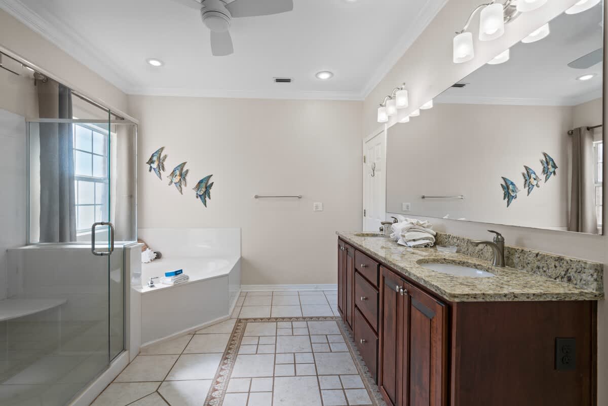 Spacious master bathroom with a double vanity featuring a granite countertop and two sinks, a large mirror, a glass-enclosed walk-in shower, and a corner jetted tub next to a window, all on a tiled floor.