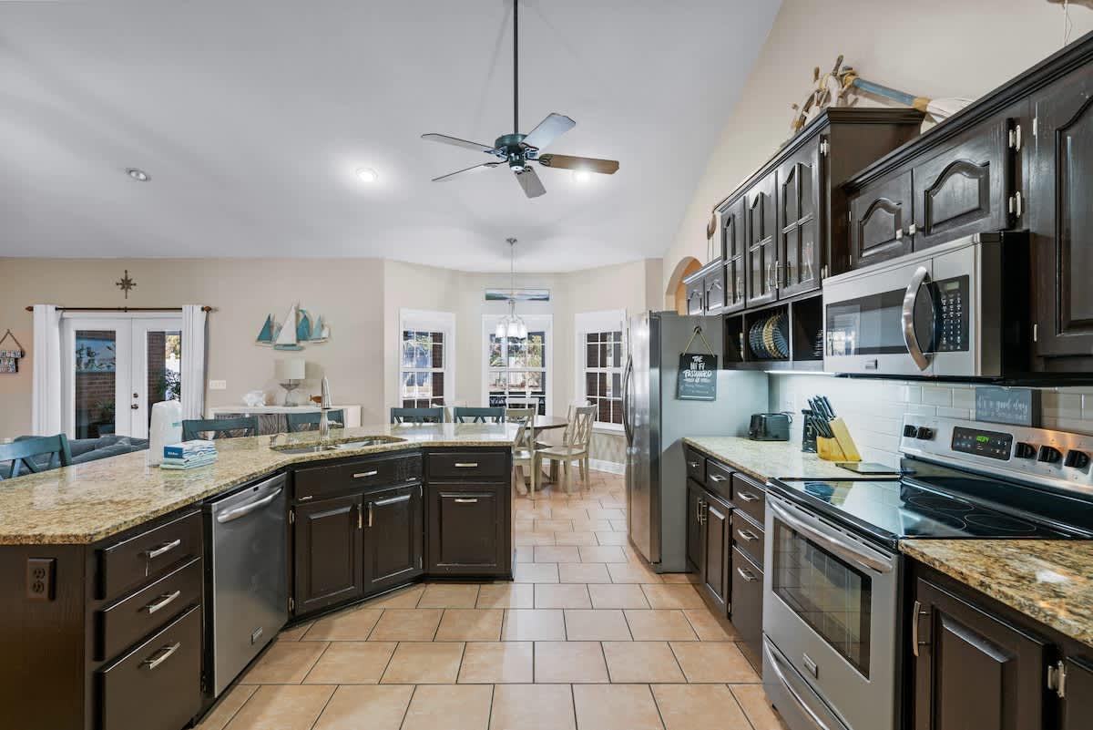 Well-equipped kitchen featuring dark wood cabinets, granite countertops, and stainless steel appliances including a refrigerator, oven, and microwave. White subway tile backsplash and light tile flooring are present.