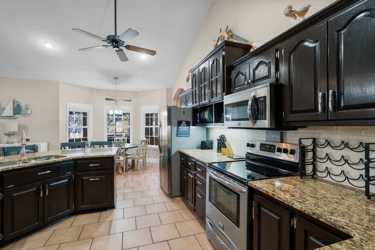 Bright kitchen with dark wood cabinetry, speckled granite countertops, and stainless steel appliances. The space features light tile flooring and a decorative wine rack above the counter.