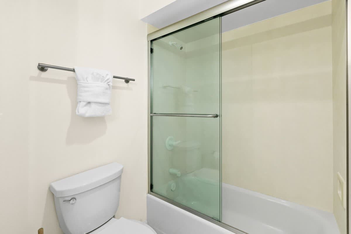 A clean, light-colored bathroom featuring a white toilet and a shower-tub combination enclosed by sliding glass doors, with a white towel hanging on a wall-mounted rack.