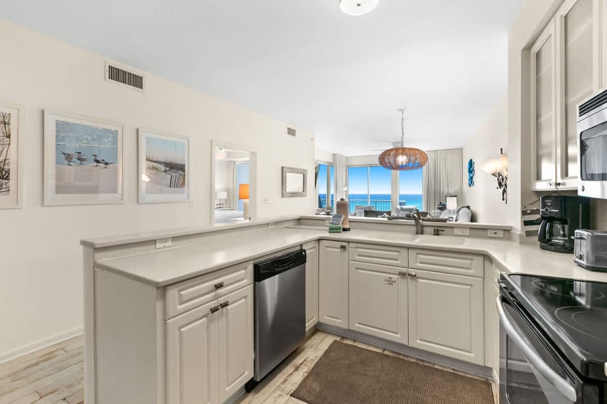 Well-equipped kitchen counter with a stainless steel dishwasher, sink, and a black electric stove, complemented by a microwave, coffee maker, and toaster.