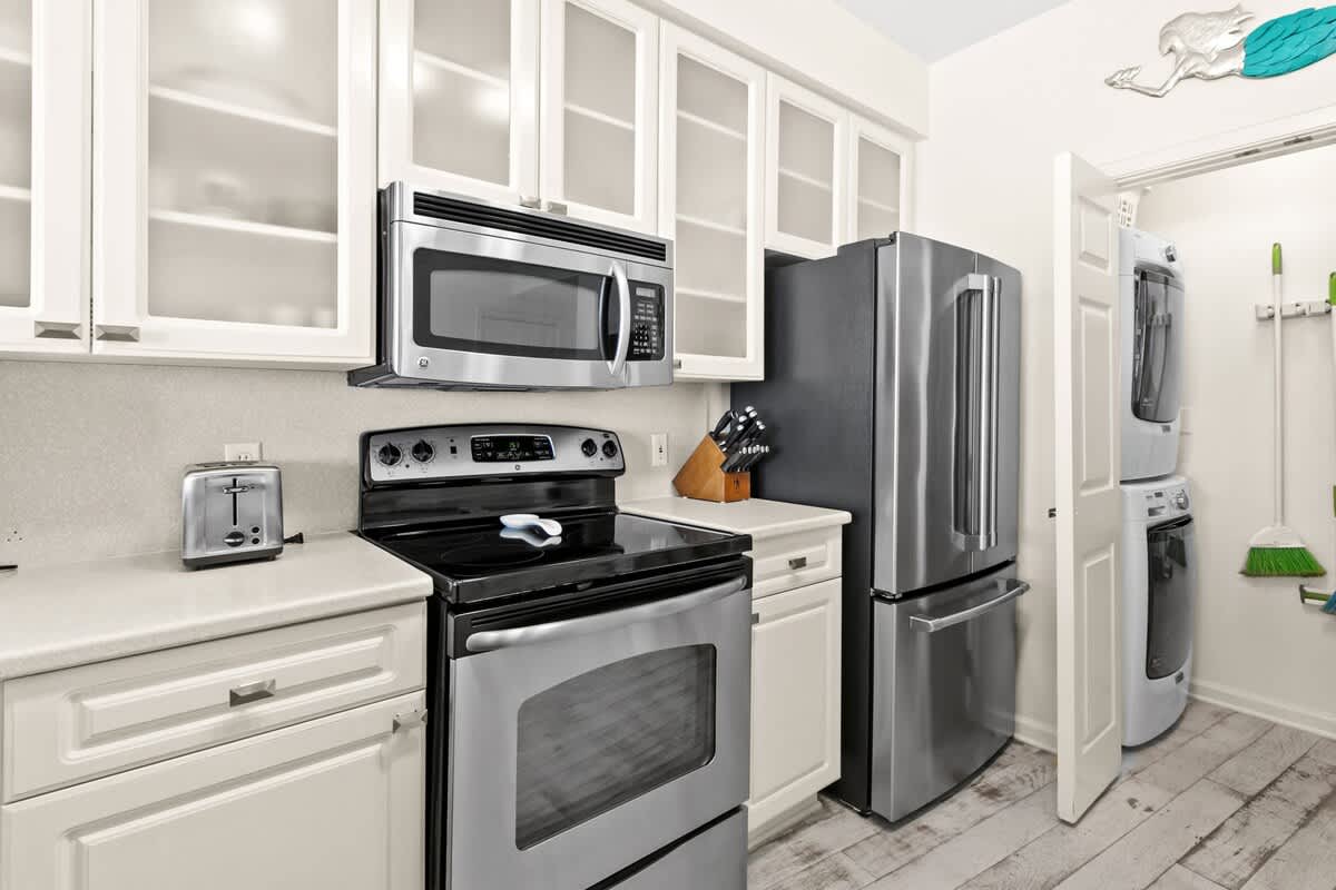 Kitchen area showcasing a stainless steel refrigerator, black electric stove, and a built-in microwave, with a convenient laundry closet housing a stacked washer and dryer.