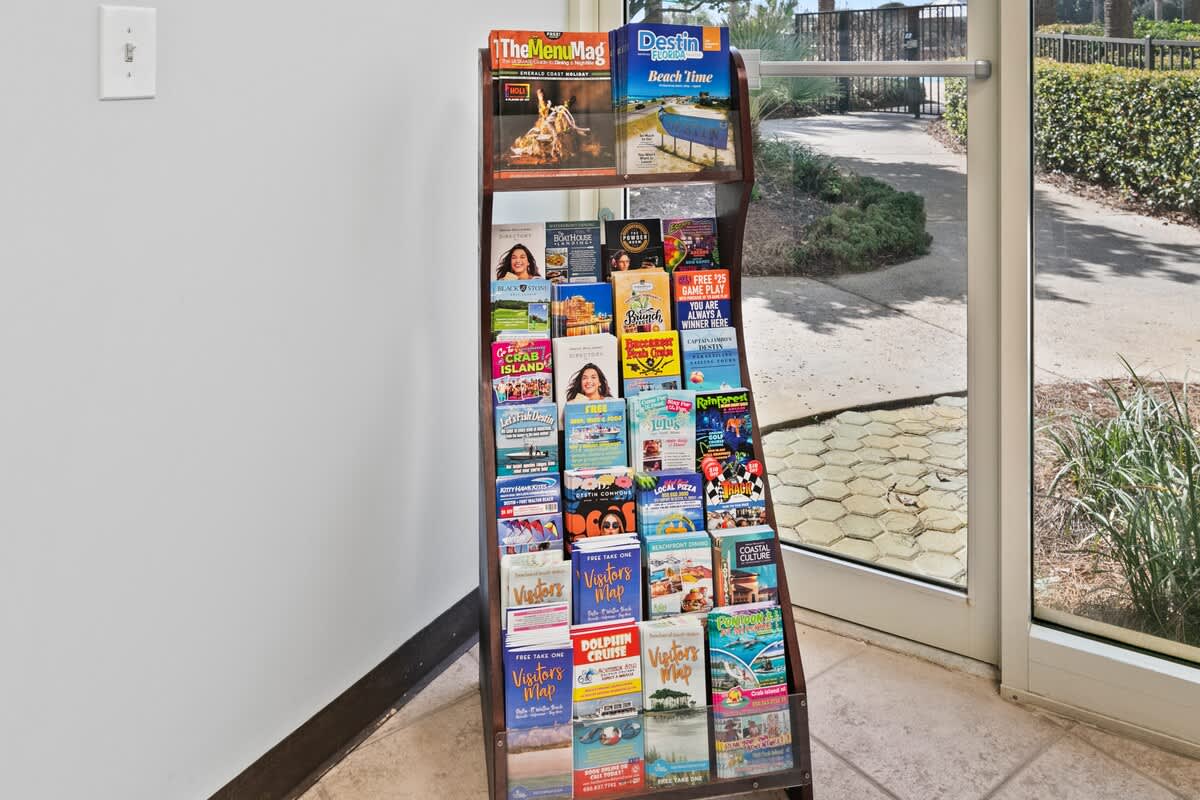 A tall wooden display rack filled with various local brochures, magazines, and visitor guides, positioned near a glass door leading to an outdoor area. The floor is light-colored tile.