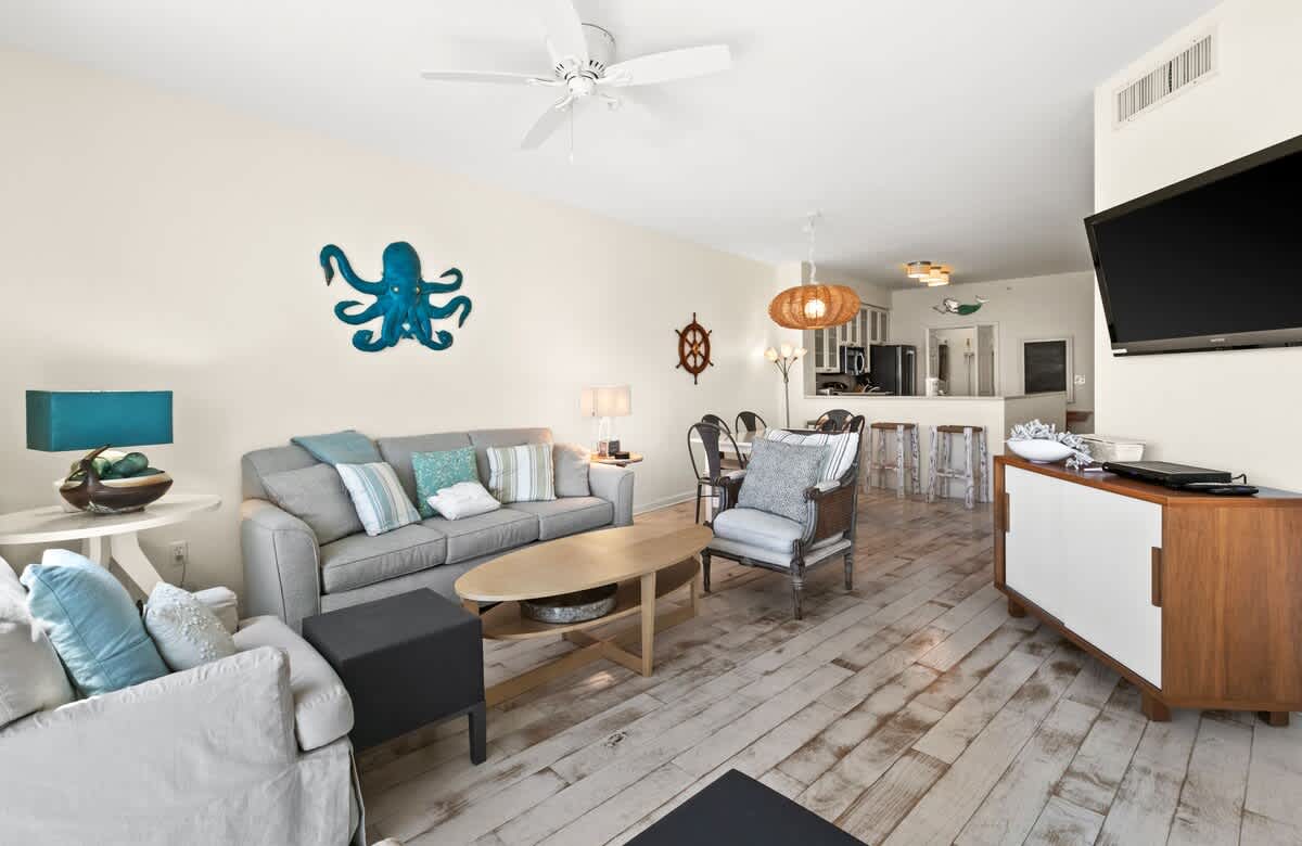 Expansive living area with a grey sofa, armchairs, and a prominent blue octopus wall decoration, flowing into the dining space and offering a bright, open feel.
