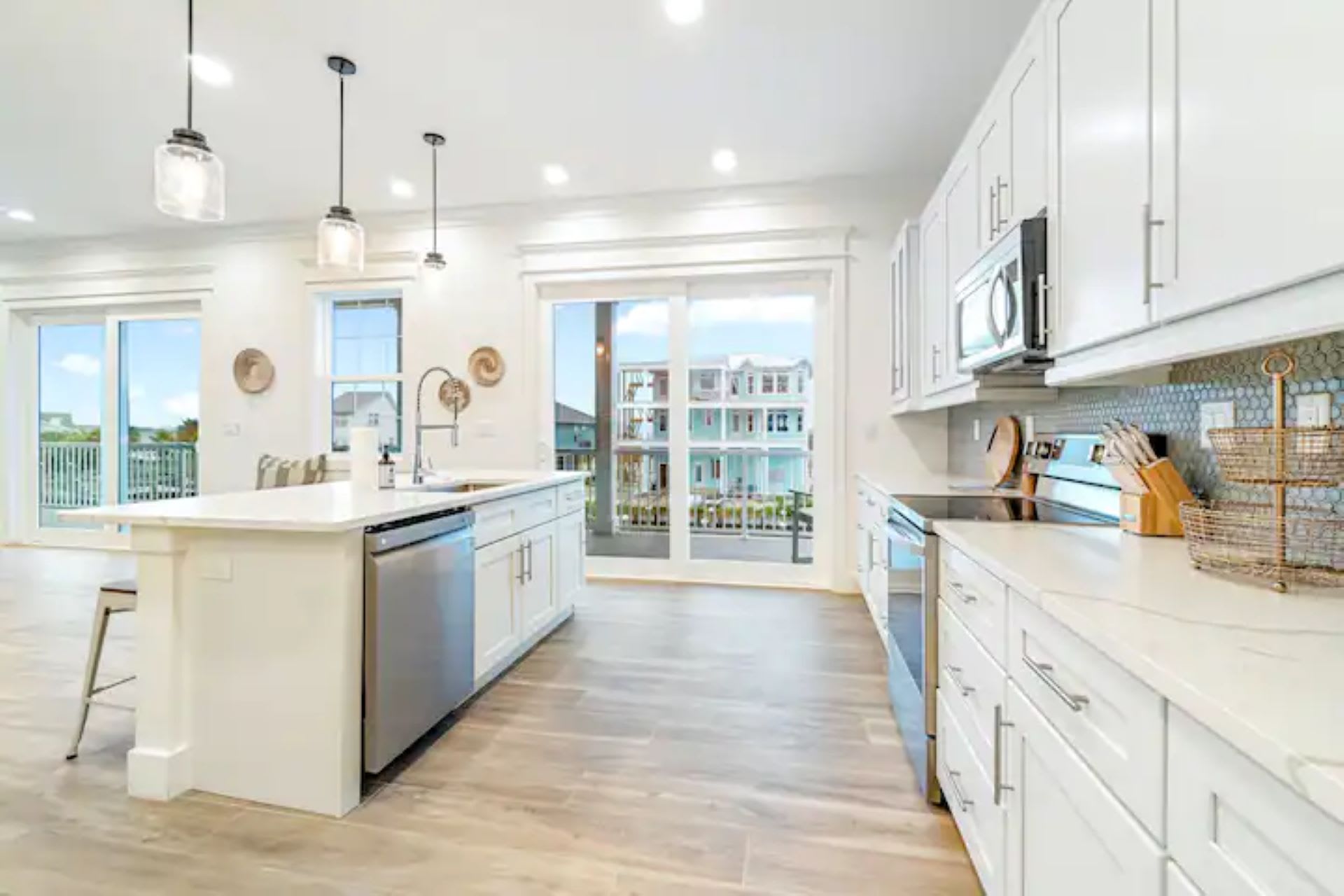 Modern kitchen with white shaker cabinets, stainless steel appliances, a large island with seating, and sliding glass doors leading to a balcony.