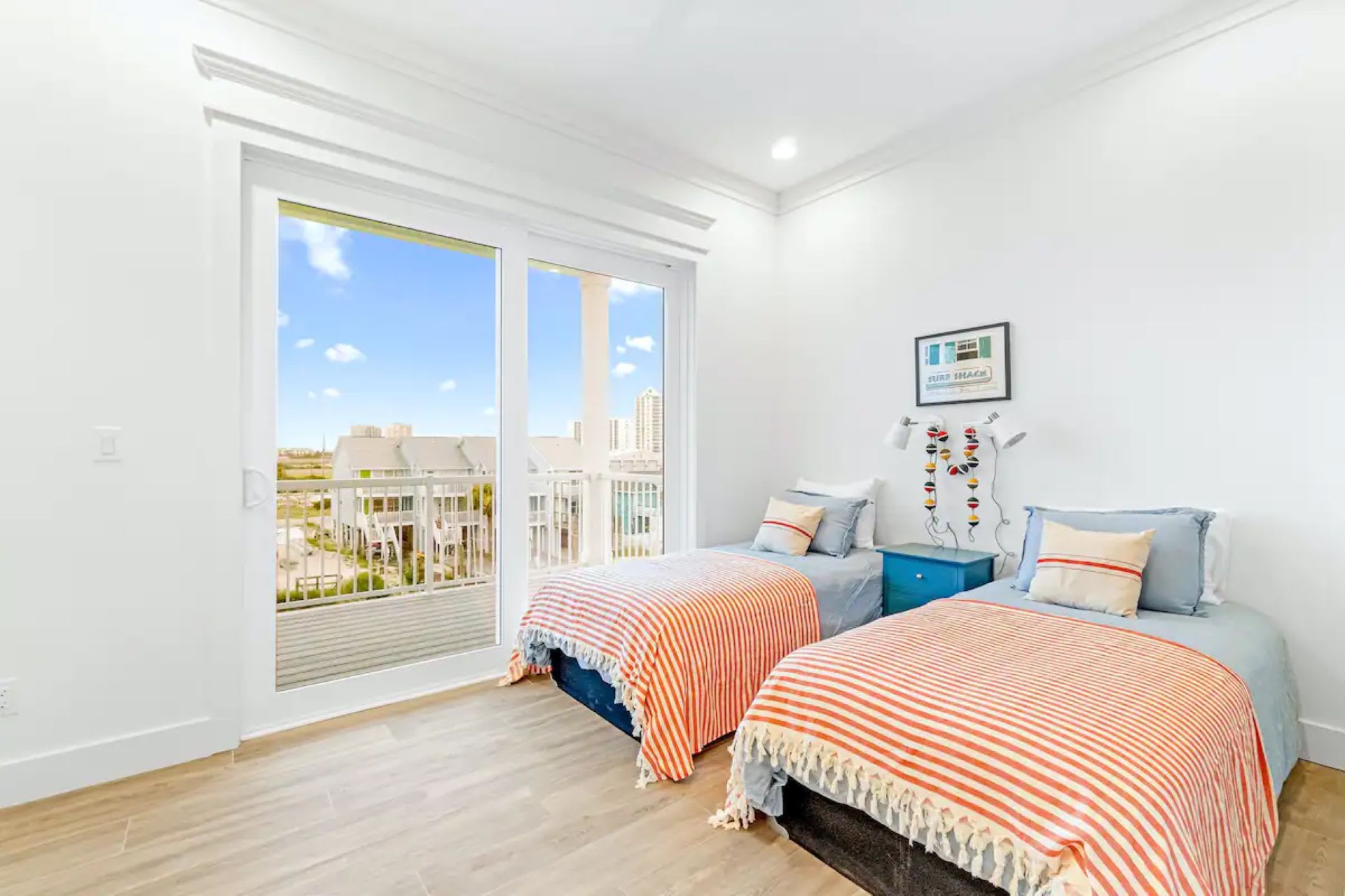 Kids' bedroom with two twin beds, colorful striped blankets, and a sliding glass door opening to a balcony with views of other properties.