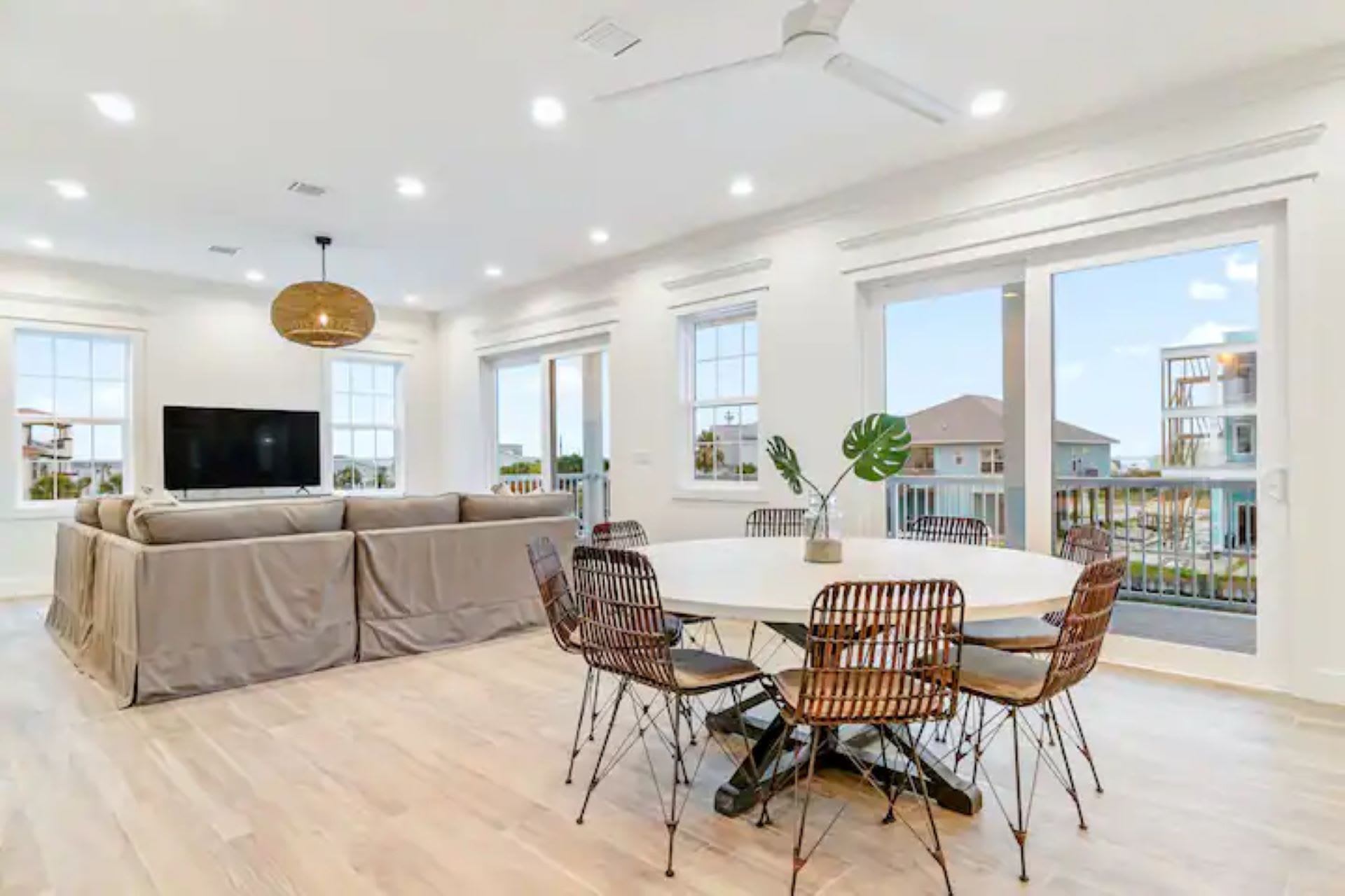 The dining area, with its round white table and woven chairs, opens to a balcony through large sliding glass doors, offering bright natural light and views of the surroundings.