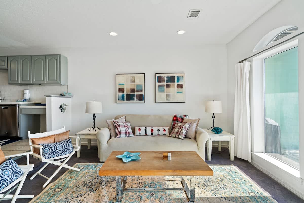 Cozy living room area with a light-colored sofa flanked by two white end tables with lamps, a wooden coffee table on a patterned rug, and two pieces of abstract artwork on the wall.
