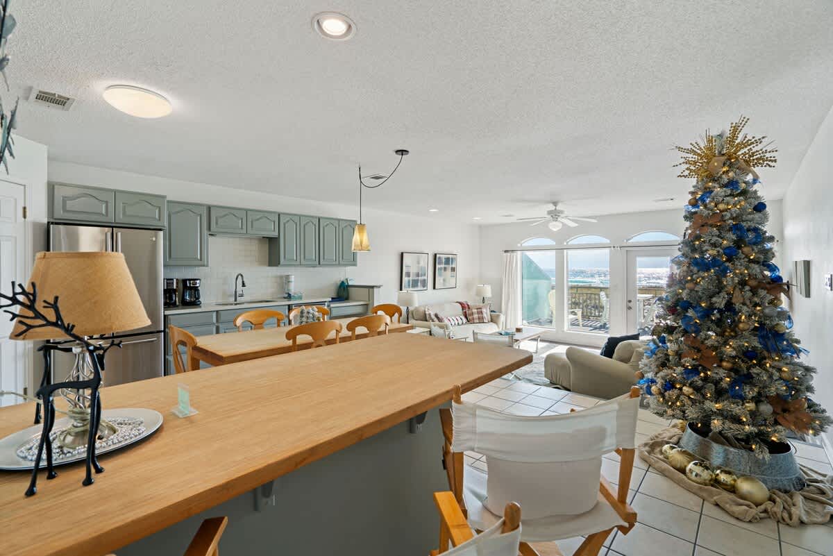 Open-concept kitchen and dining area with light blue cabinets, stainless steel appliances, and a large wooden island, extending into a living room with a Christmas tree and ocean views.