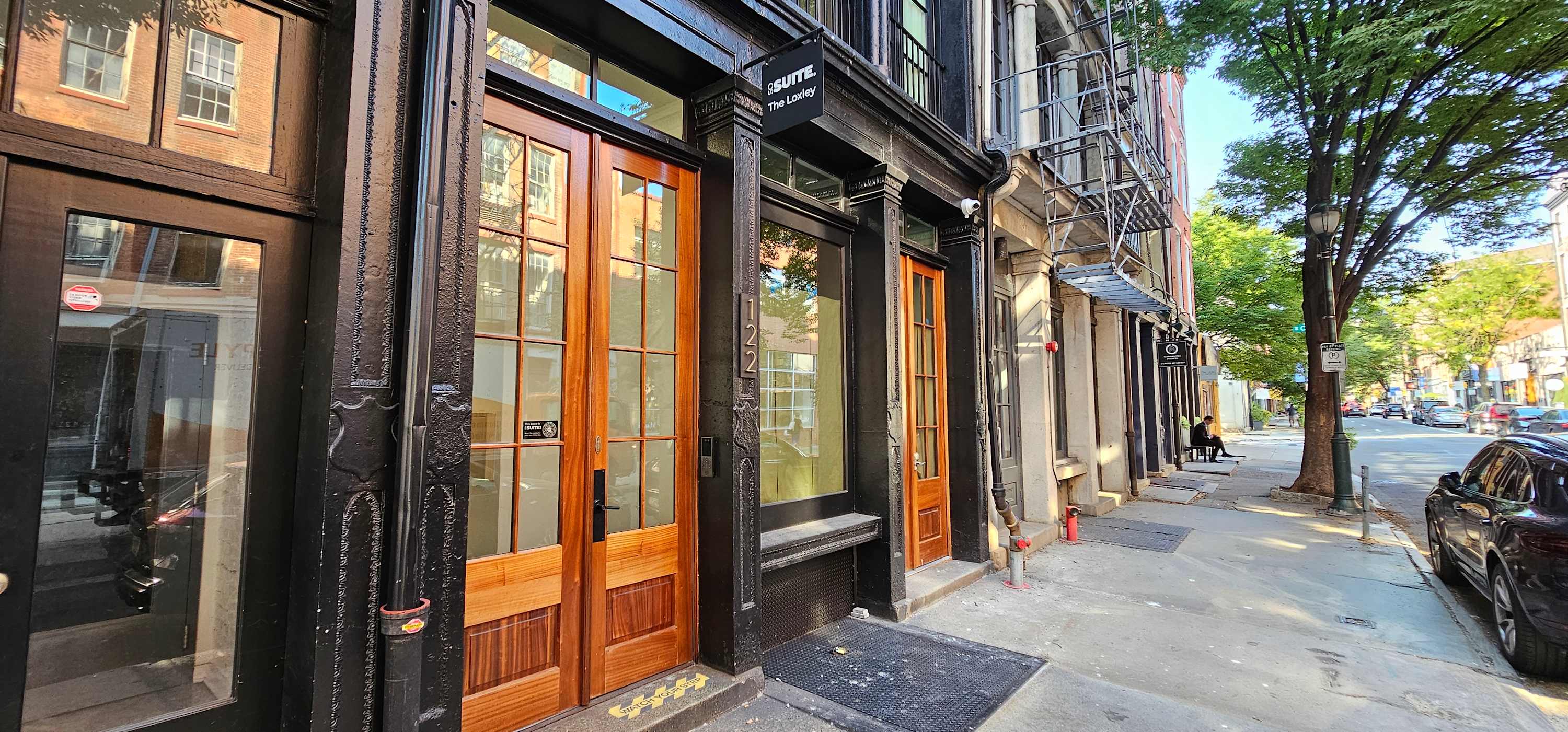 Street view of the building's dark-colored facade, featuring large wooden double doors and multiple windows, with a prominent 'Sosuite' sign above the entrance.