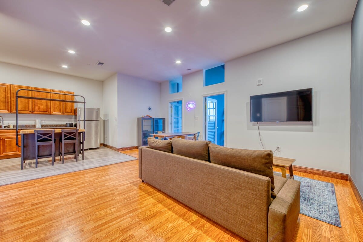 Spacious open-concept living area with a brown sectional sofa, leading into the dining space and kitchen. Recessed lighting illuminates the room with warm light.