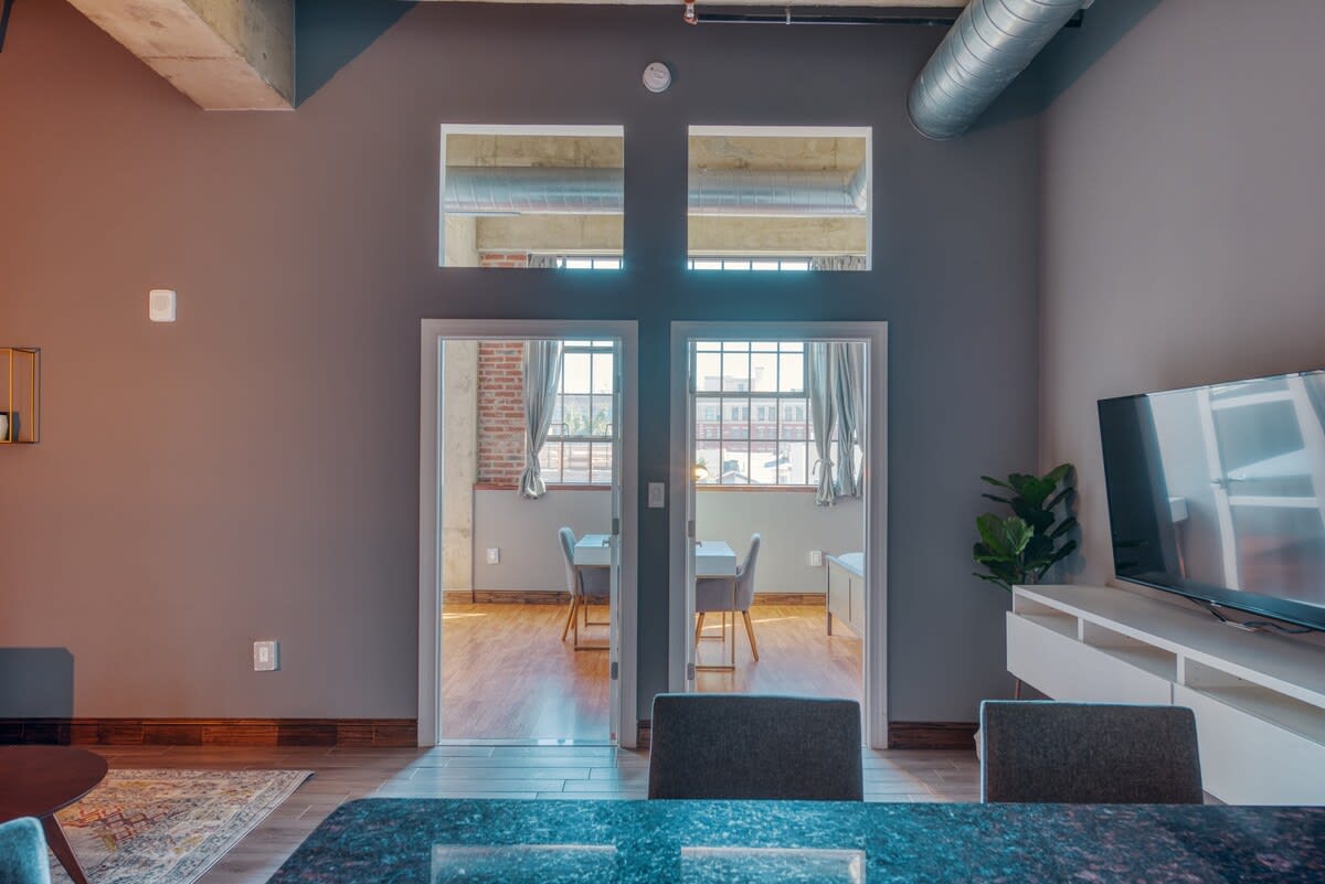 A view from the living area towards two rooms accessible through double glass-paned doors, with open transom windows above, revealing a desk and chair in the room beyond.
