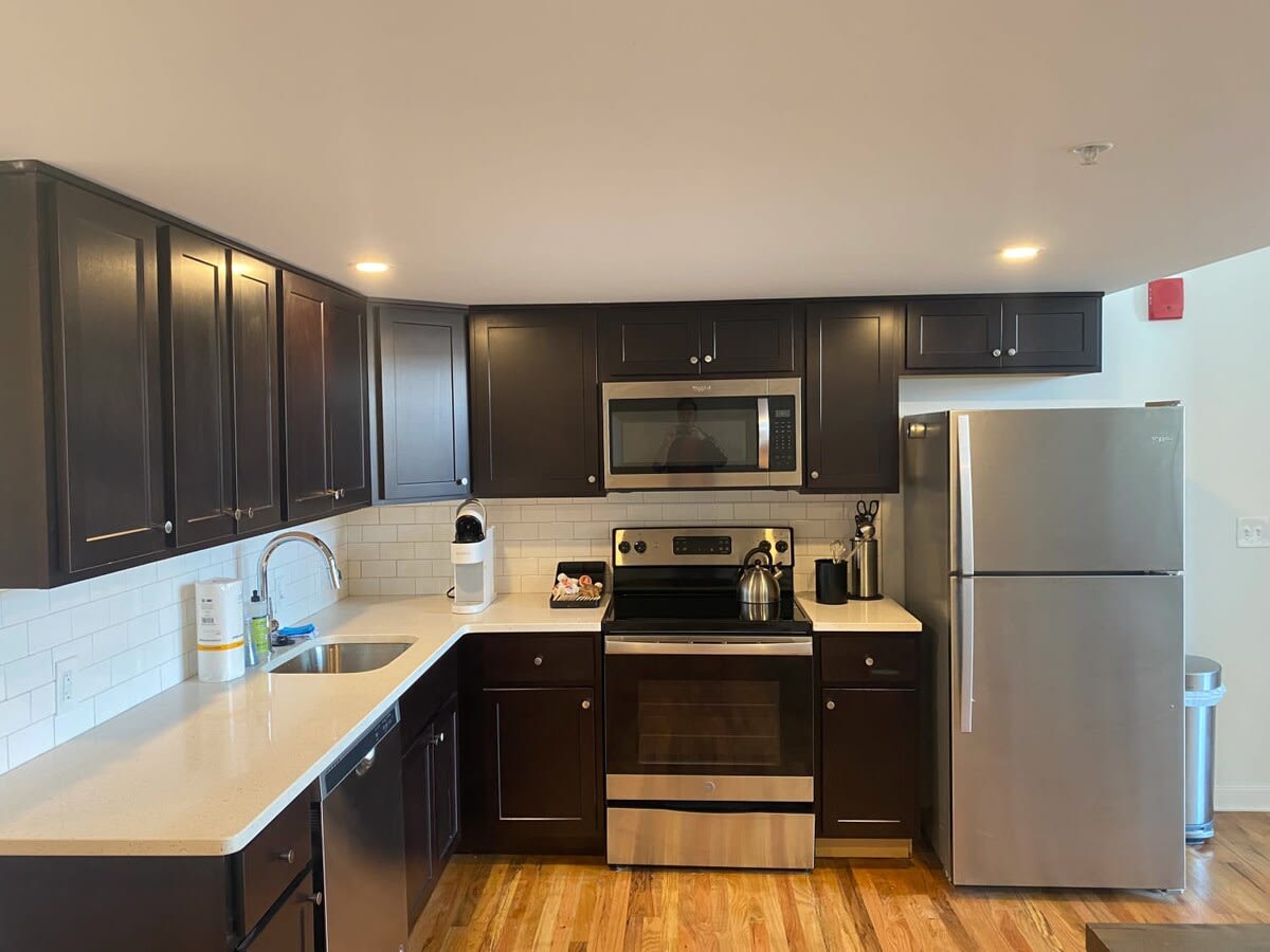 Modern U-shaped kitchen with dark wood shaker cabinets, light quartz countertops, a white subway tile backsplash, and stainless steel appliances including a refrigerator, oven, microwave, and dishwasher.