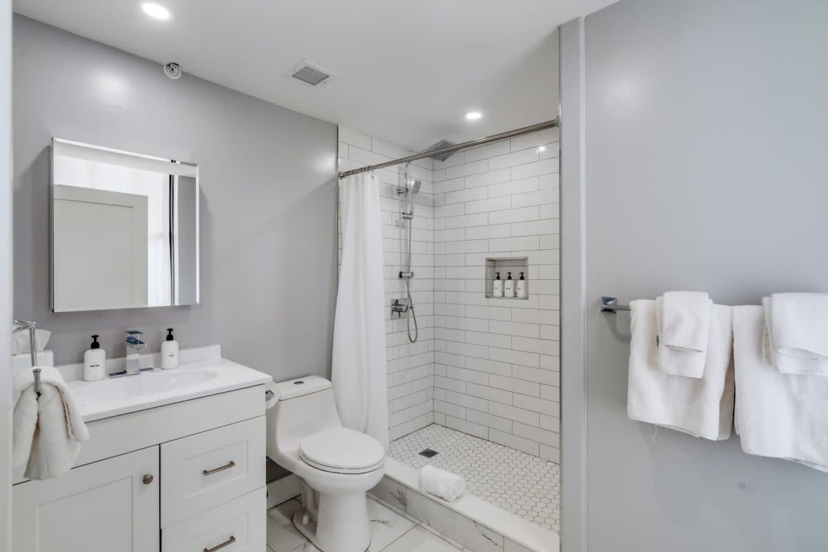 Contemporary bathroom with a white vanity and sink, a toilet, and a walk-in shower featuring white subway tiles and a hexagonal tile floor.