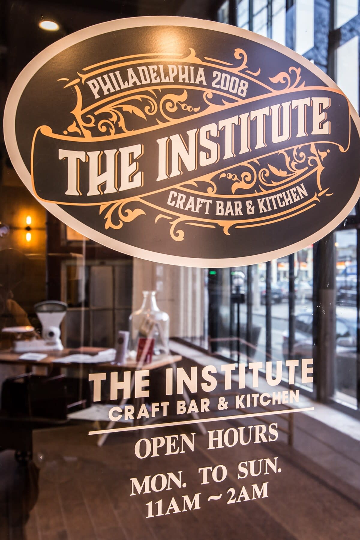 Close-up of a vintage-style glass sign for "The Institute Craft Bar & Kitchen" with "Open Hours Mon. to Sun. 11AM ~ 2AM" visible below.