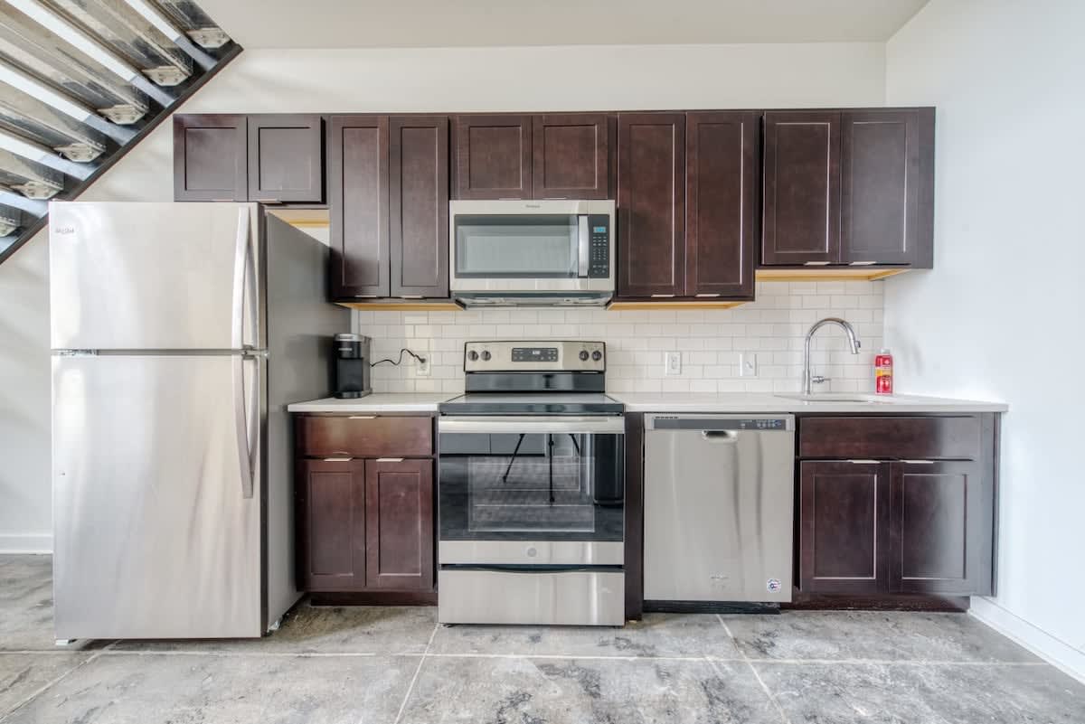 Modern kitchen featuring dark brown shaker-style cabinetry, stainless steel appliances including a refrigerator, range, microwave, and dishwasher, complemented by a white subway tile backsplash and concrete flooring.