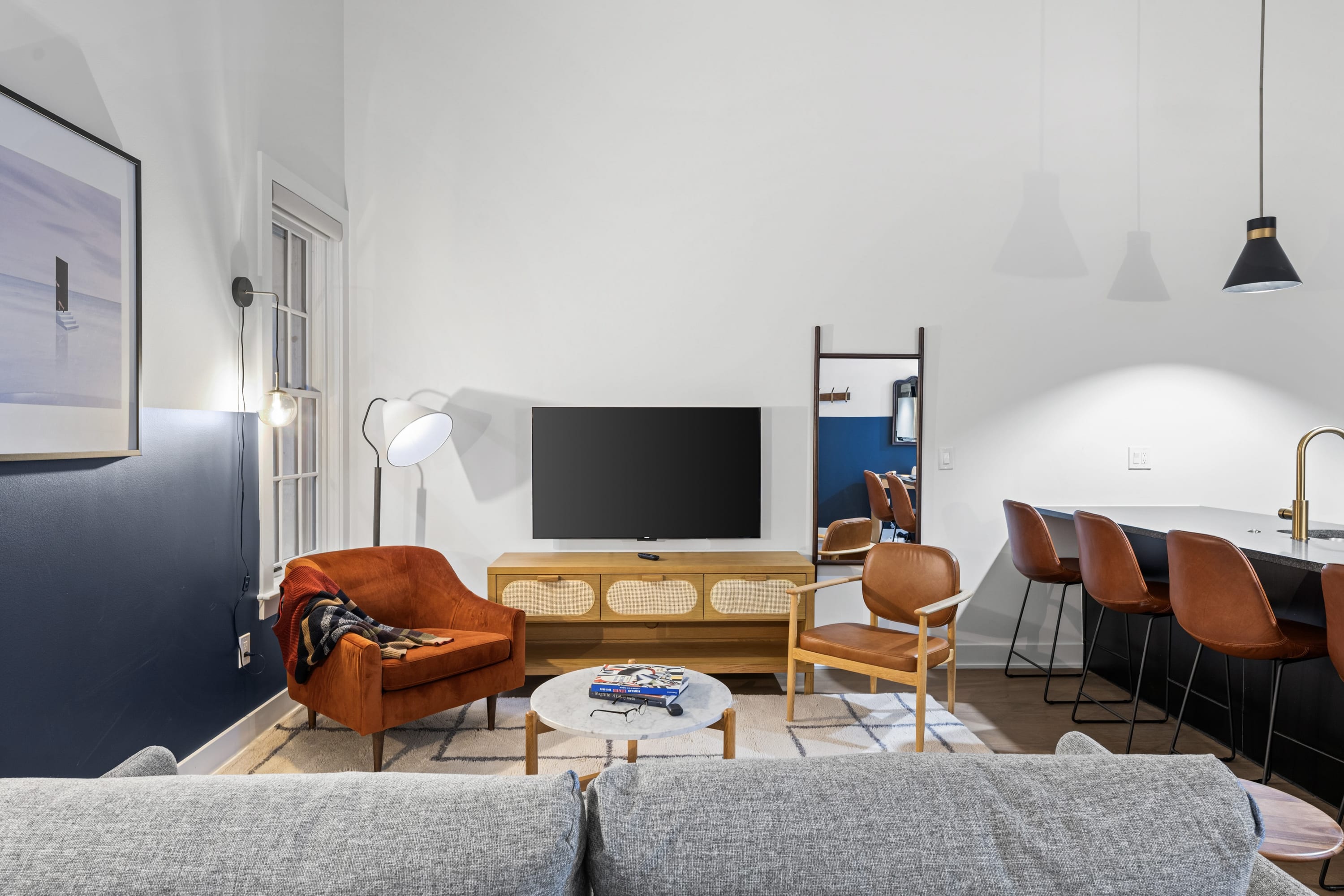 View of the living area from behind the sofa, showcasing a flat-screen TV on a wooden console, an inviting orange armchair, and a round coffee table on a patterned rug.