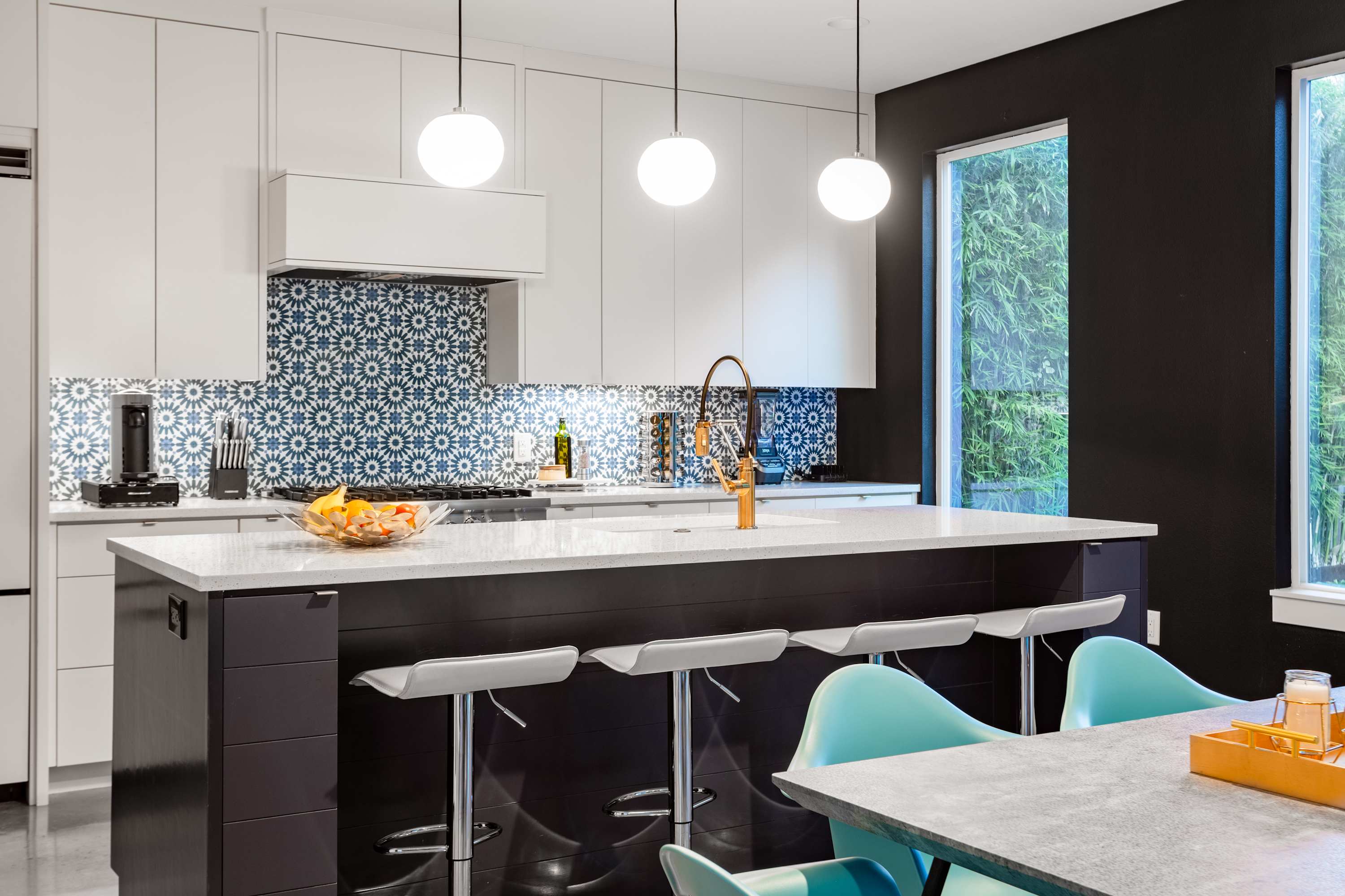 A close-up view of the modern kitchen island with a white countertop and dark cabinetry, featuring three bar stools. The blue and white patterned backsplash and gold-toned faucet add a stylish touch.