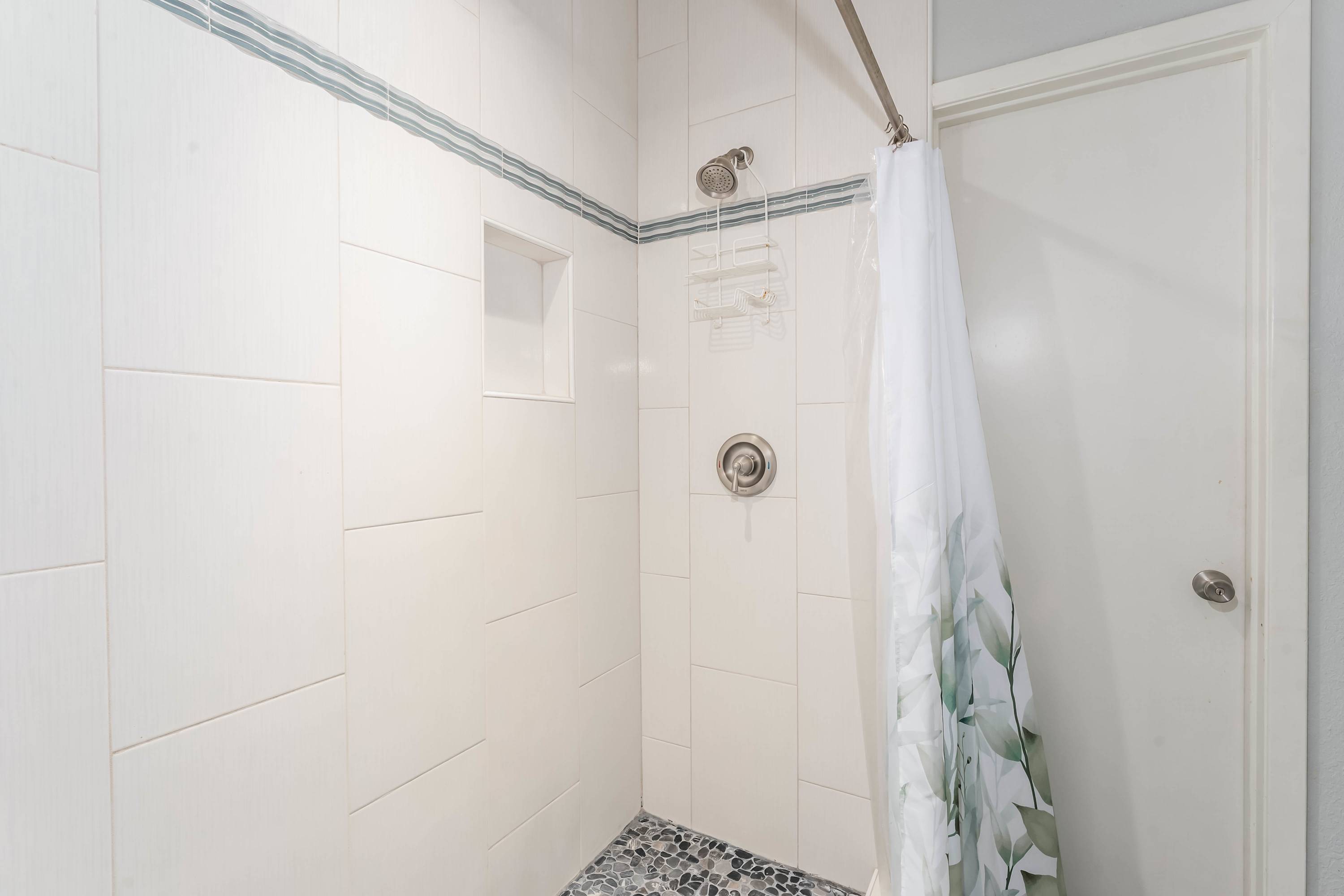 Modern shower with white subway tiles, a decorative blue stripe, and a dark pebble-stone floor, featuring a built-in niche and a rain showerhead.