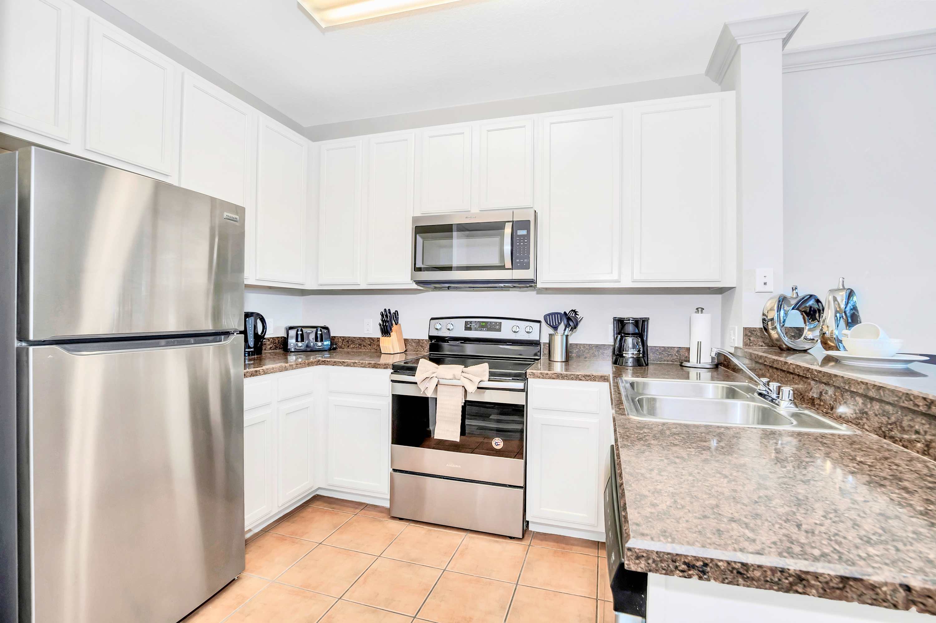 Fully equipped kitchen featuring white shaker-style cabinets, dark granite countertops, and stainless steel appliances including a refrigerator, oven, and microwave. Tiled flooring completes the space.