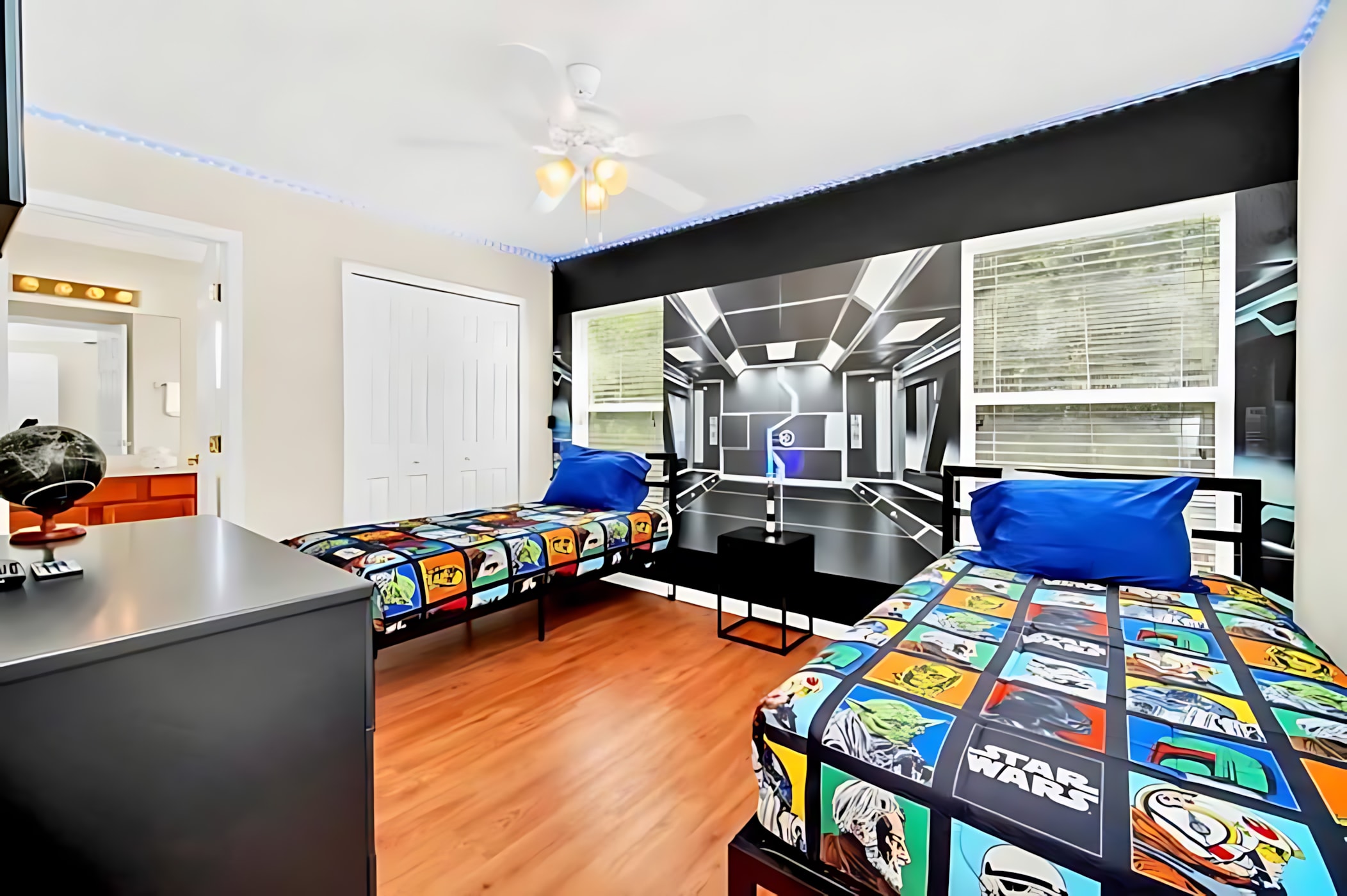 Themed bedroom featuring two twin beds with Star Wars character bedding, a large wall mural depicting a futuristic corridor, and a ceiling fan with blue LED strip lighting.