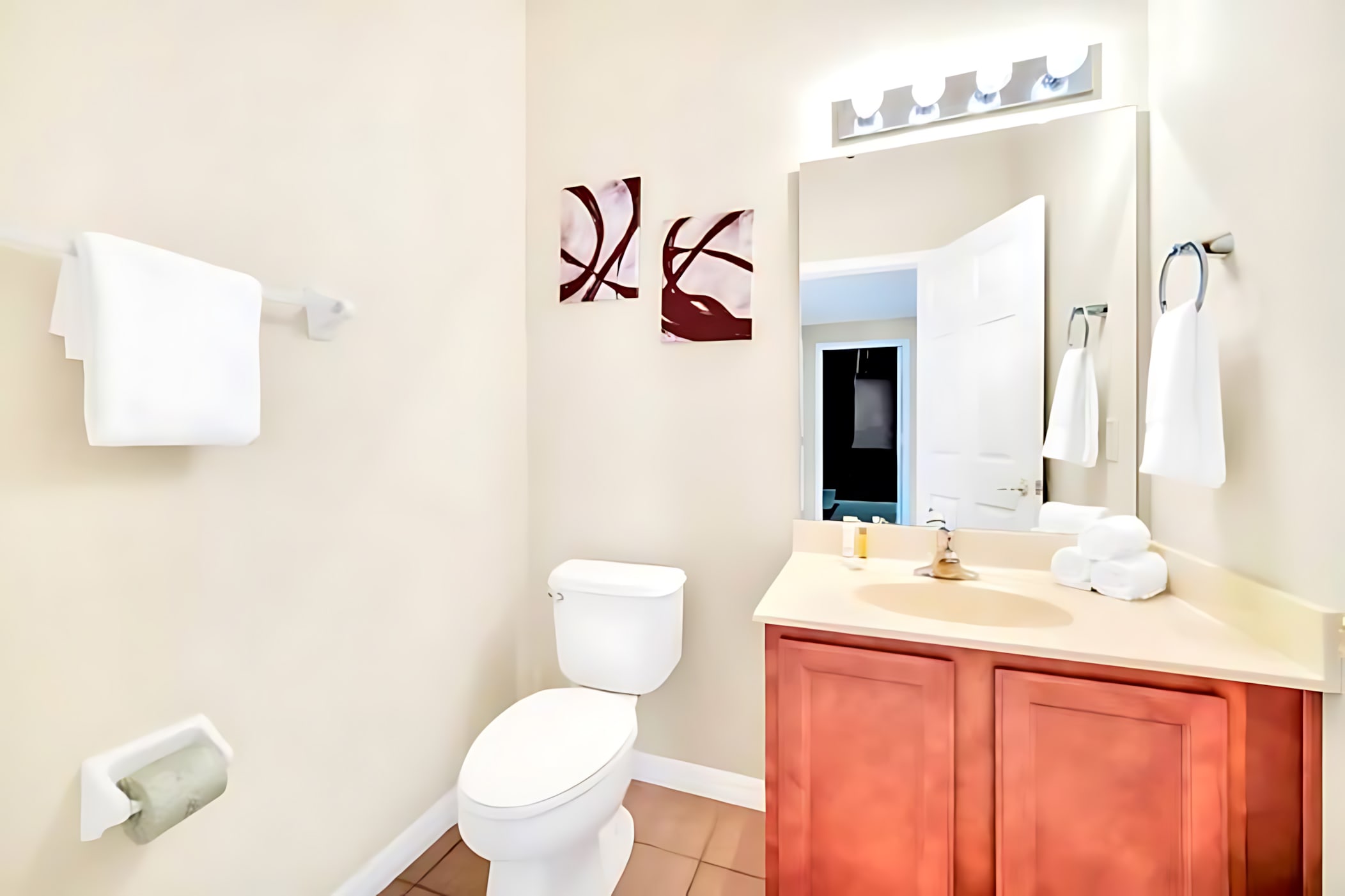 Compact bathroom featuring a single wood vanity with a light countertop, a mirror, toilet, and simple wall art, with white towels neatly folded.