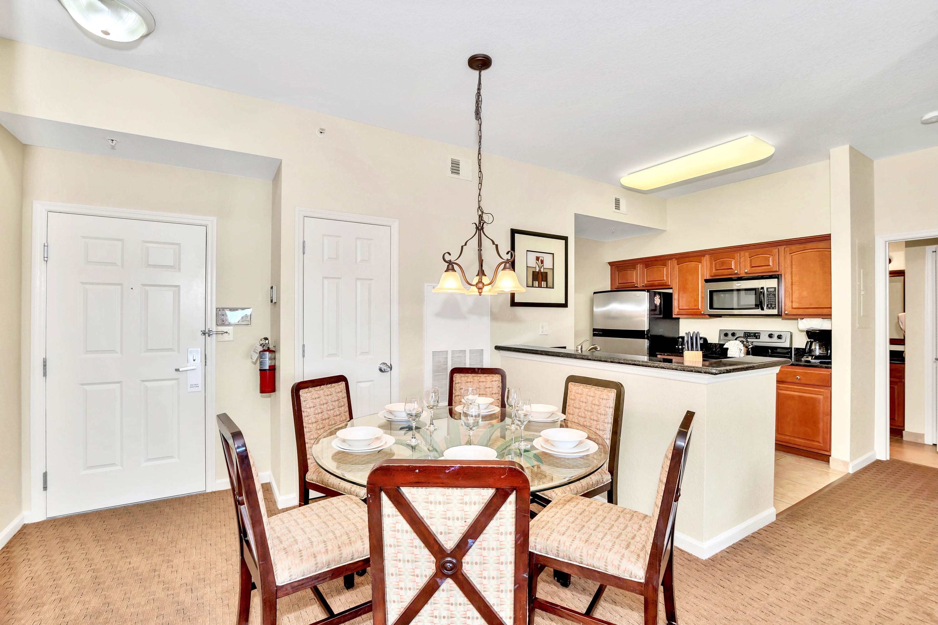 The dining area features a round glass-top table with six upholstered chairs under a decorative chandelier, adjacent to a modern kitchen with wood cabinetry, granite countertops, and stainless steel appliances.