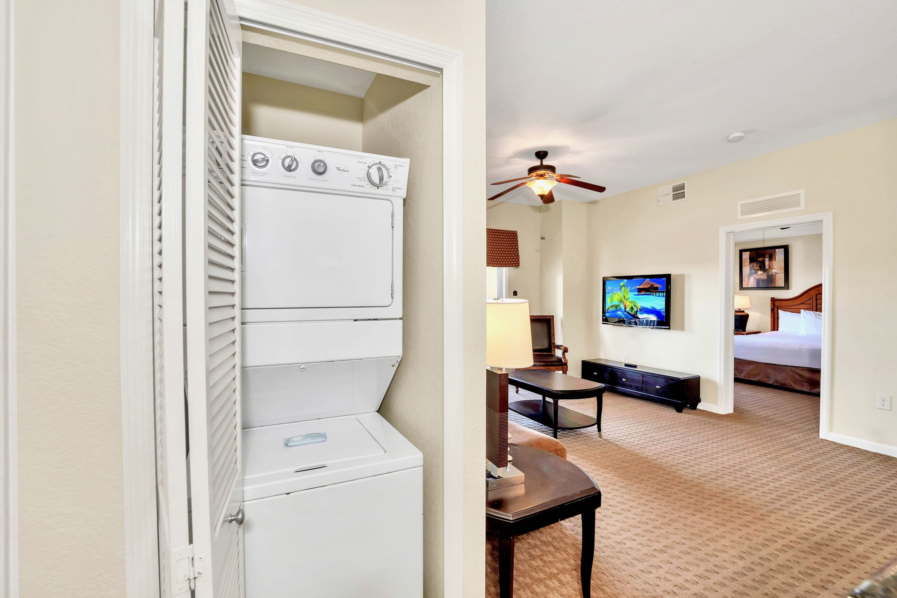 Compact laundry closet featuring a stacked white washer and dryer unit with louvered bifold doors, located near the living area.