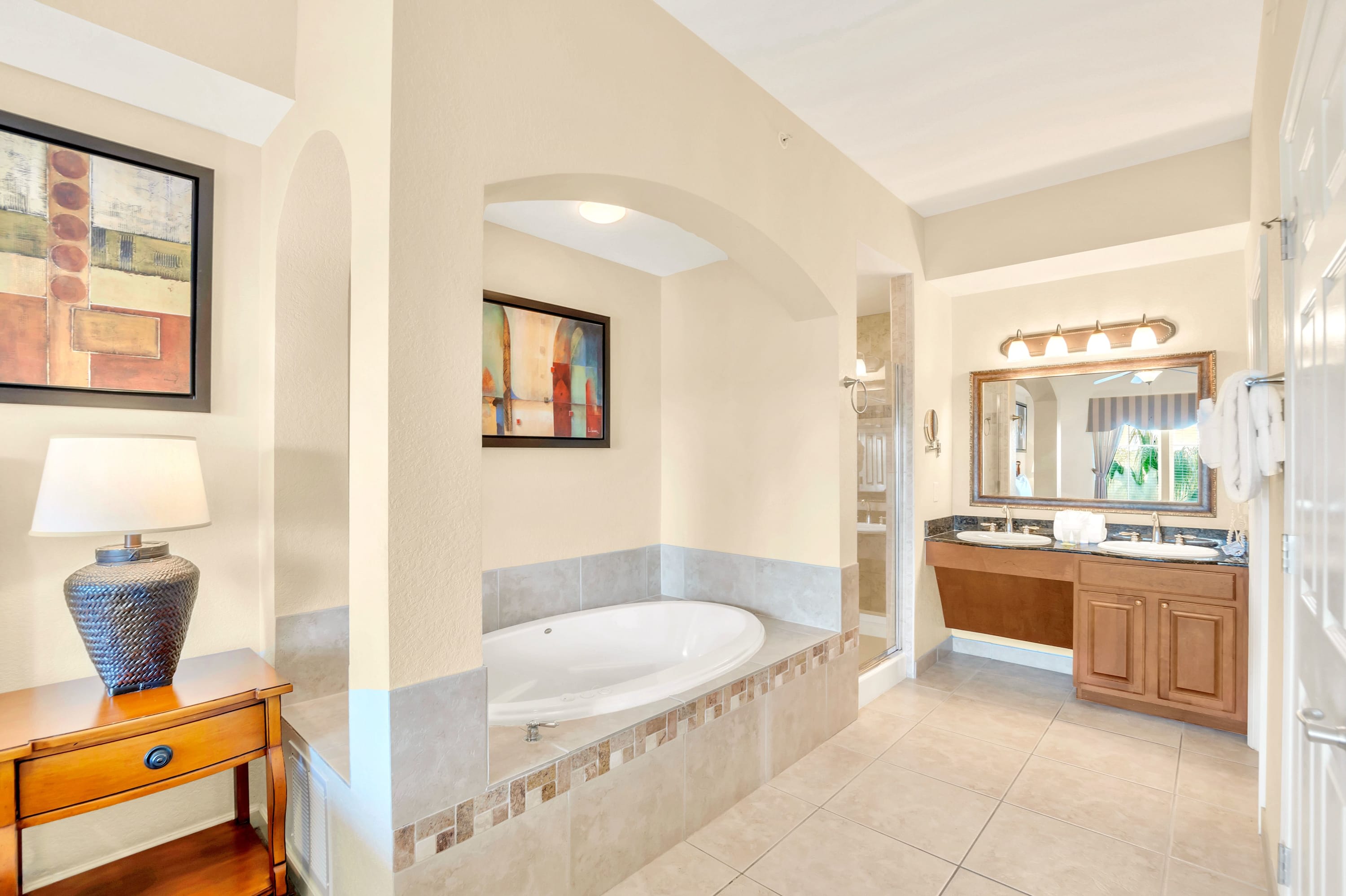Expansive master bathroom with a jetted tub in an arched alcove, and a double vanity with dark wood cabinets and granite countertops, reflected in a large ornate mirror.