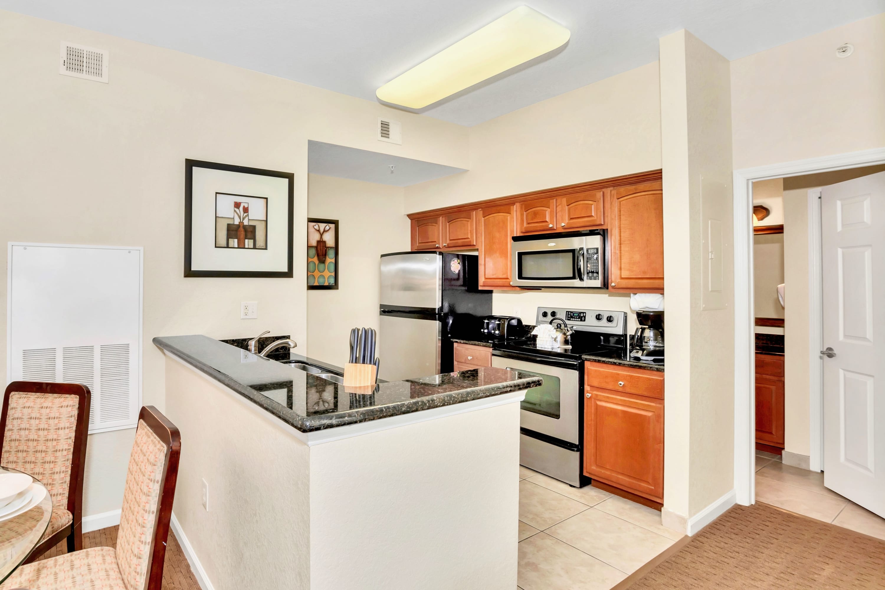 Modern kitchen with light wood cabinets, black granite countertops, and stainless steel appliances, featuring a breakfast bar with seating and tile flooring.