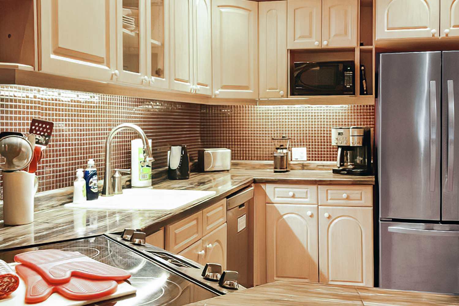 Detailed view of the kitchen counter area with light wood cabinetry, a dark tiled backsplash, and various small appliances like a toaster and coffee maker. A stainless steel refrigerator and dishwasher are also visible.
