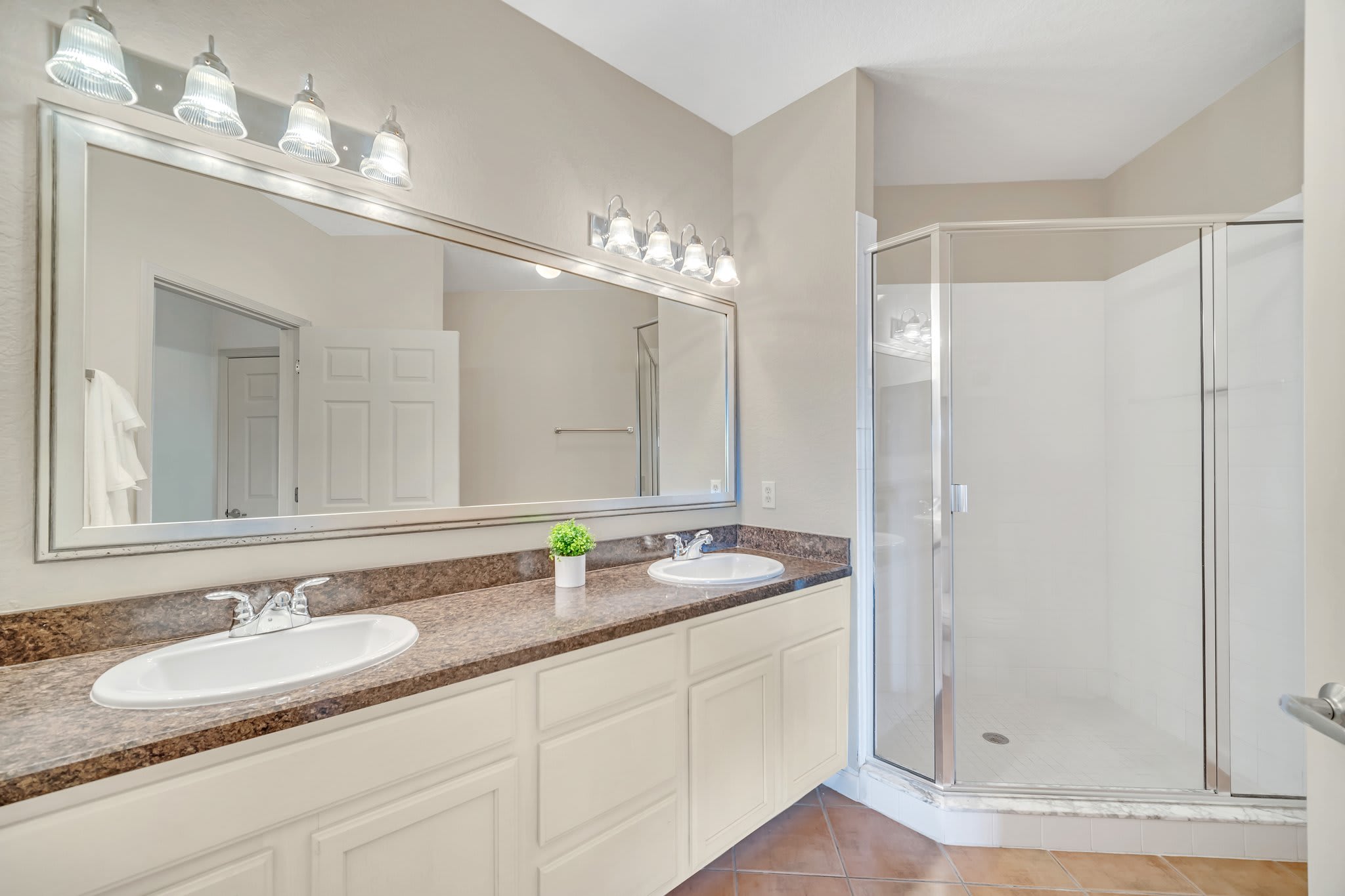 Master bathroom with a long double vanity featuring white sinks, a dark speckled countertop, and white cabinets. A large framed mirror with sconce lighting is above, next to a glass-enclosed walk-in shower.