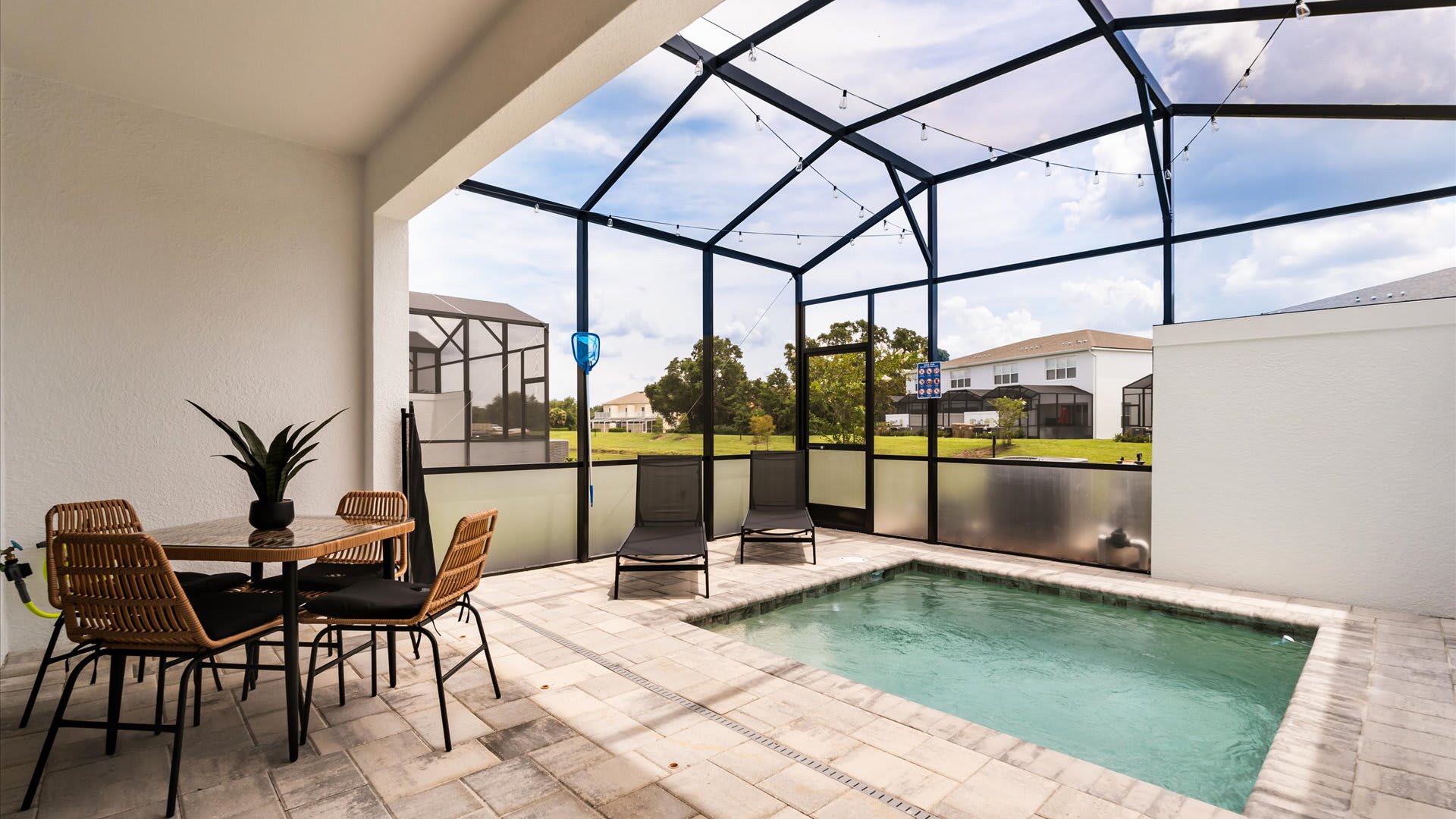 Screened-in outdoor patio featuring a small rectangular pool, two lounge chairs, and a dining set with a glass-top table and wicker chairs, all under a string of lights.