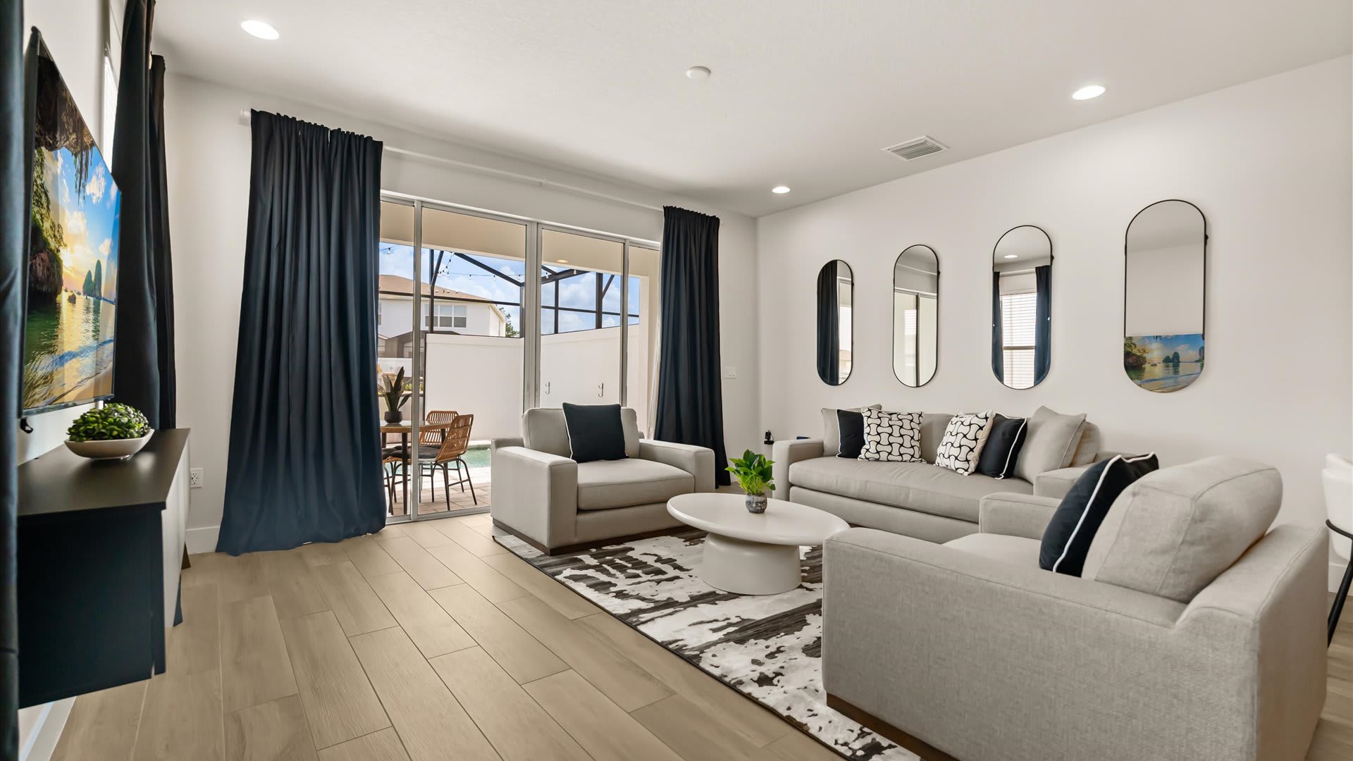 Bright living room with light gray sofas and armchairs, a white coffee table, and a patterned rug, with large sliding doors providing access to the outdoor screened patio.