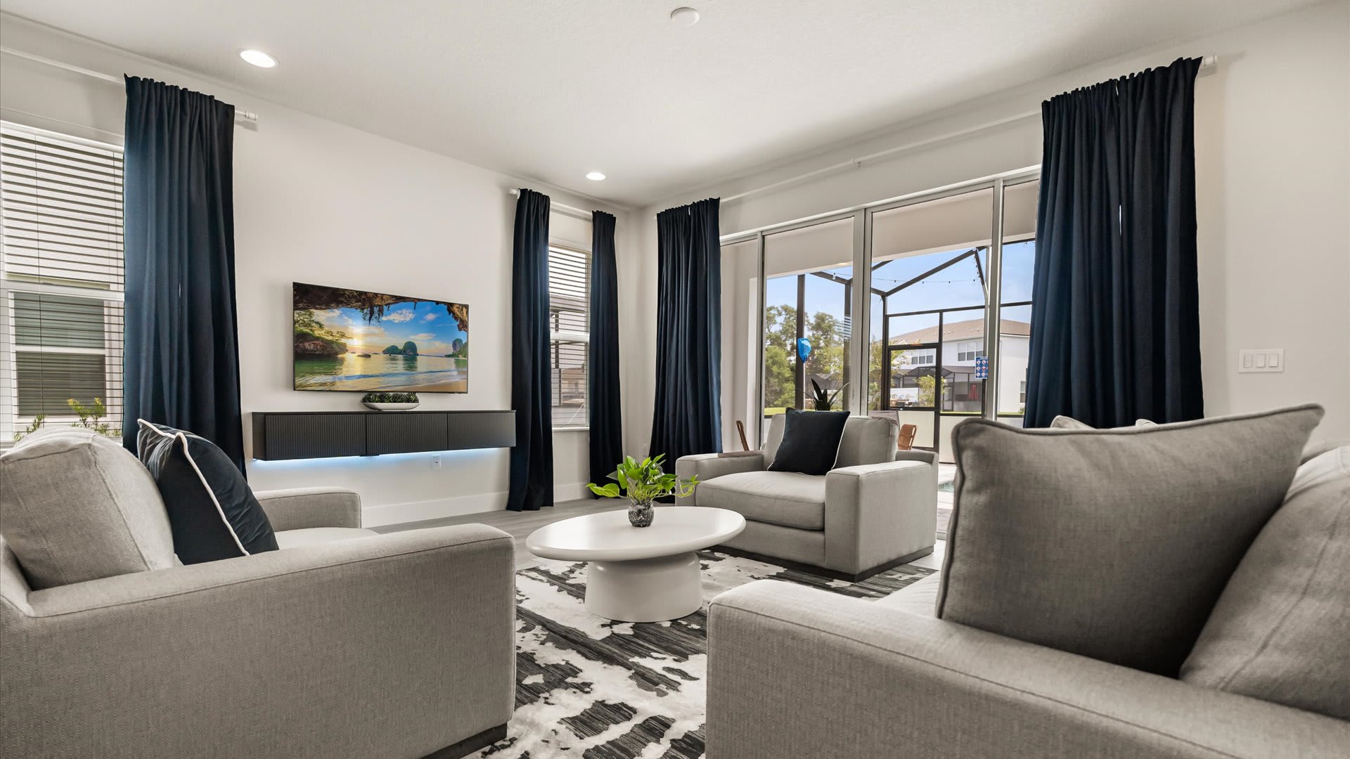 Contemporary living room with light gray seating, a wall-mounted television above a floating console, and large sliding glass doors opening to the screened patio and pool area.