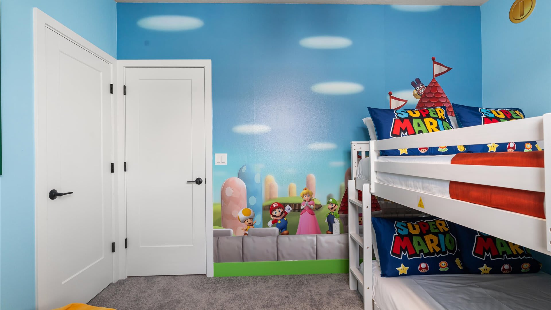 Another view of the Super Mario themed bedroom, showcasing a vibrant mural of Mario characters on the light blue wall. A white bunk bed with themed pillows and a green baseboard add to the playful design.