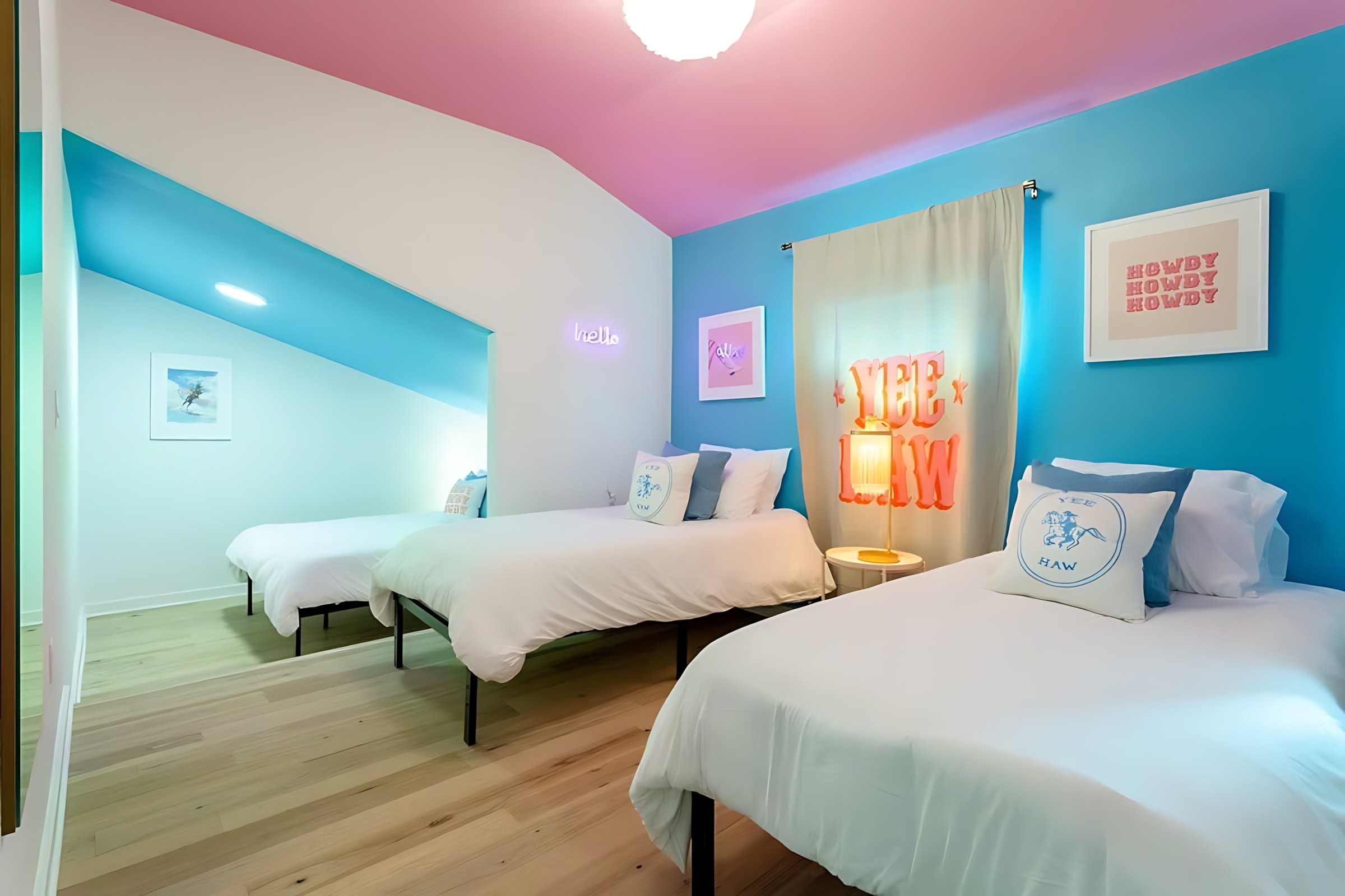 A vibrant bedroom featuring two twin beds with white bedding and blue accent pillows, set against bright blue walls and a pink sloped ceiling. Large curtains with "YEE HAW" text hang by the windows.
