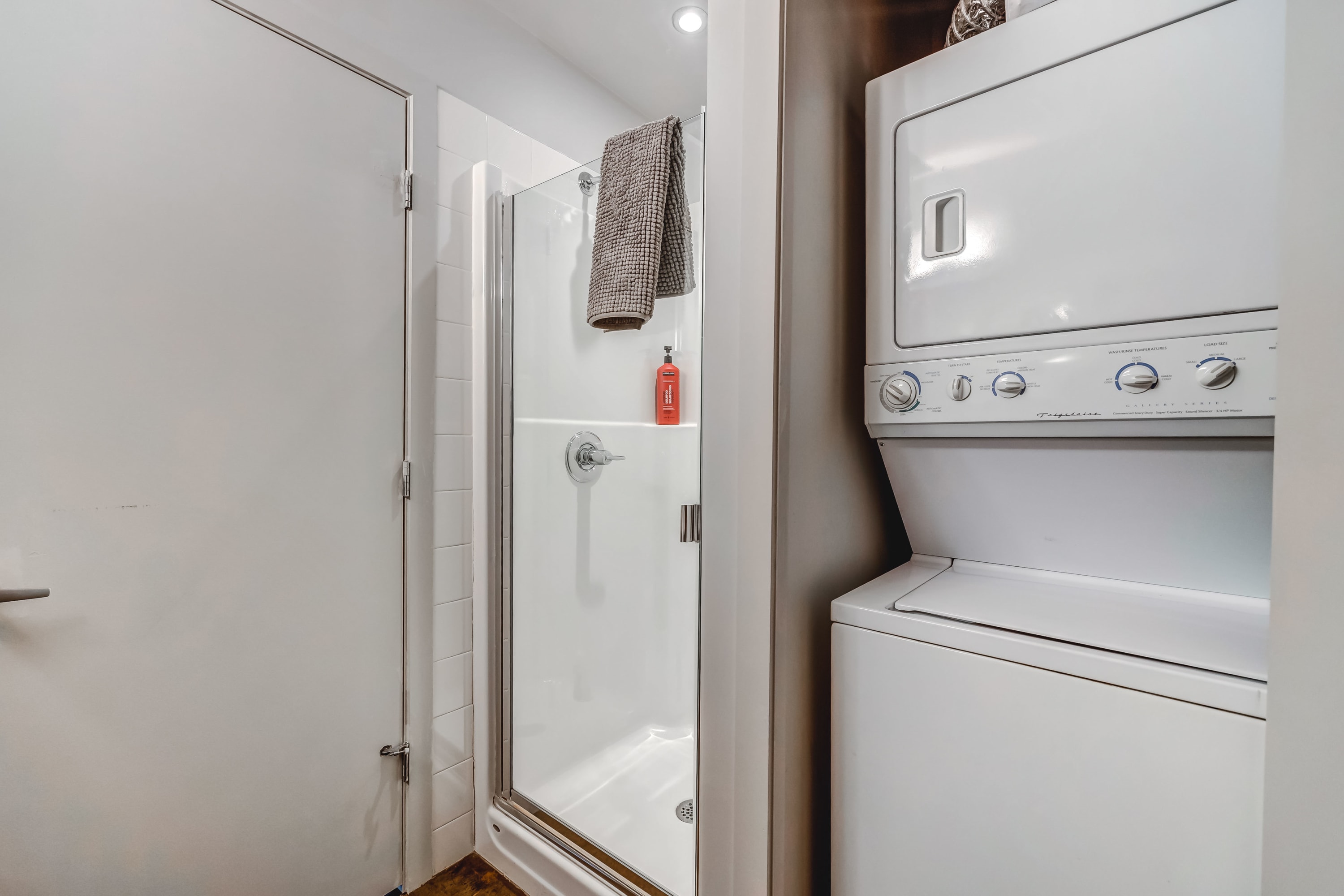 Compact bathroom area featuring a glass-enclosed shower with white subway tiles and a stacked washer and dryer unit. The space is functional and efficiently designed.