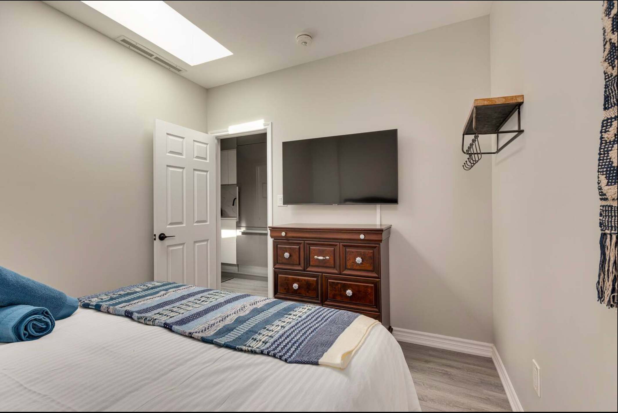 View of the second bedroom showing a wall-mounted flat-screen TV above a dark wood dresser, with an open door revealing a walk-in closet, and a skylight providing natural light.
