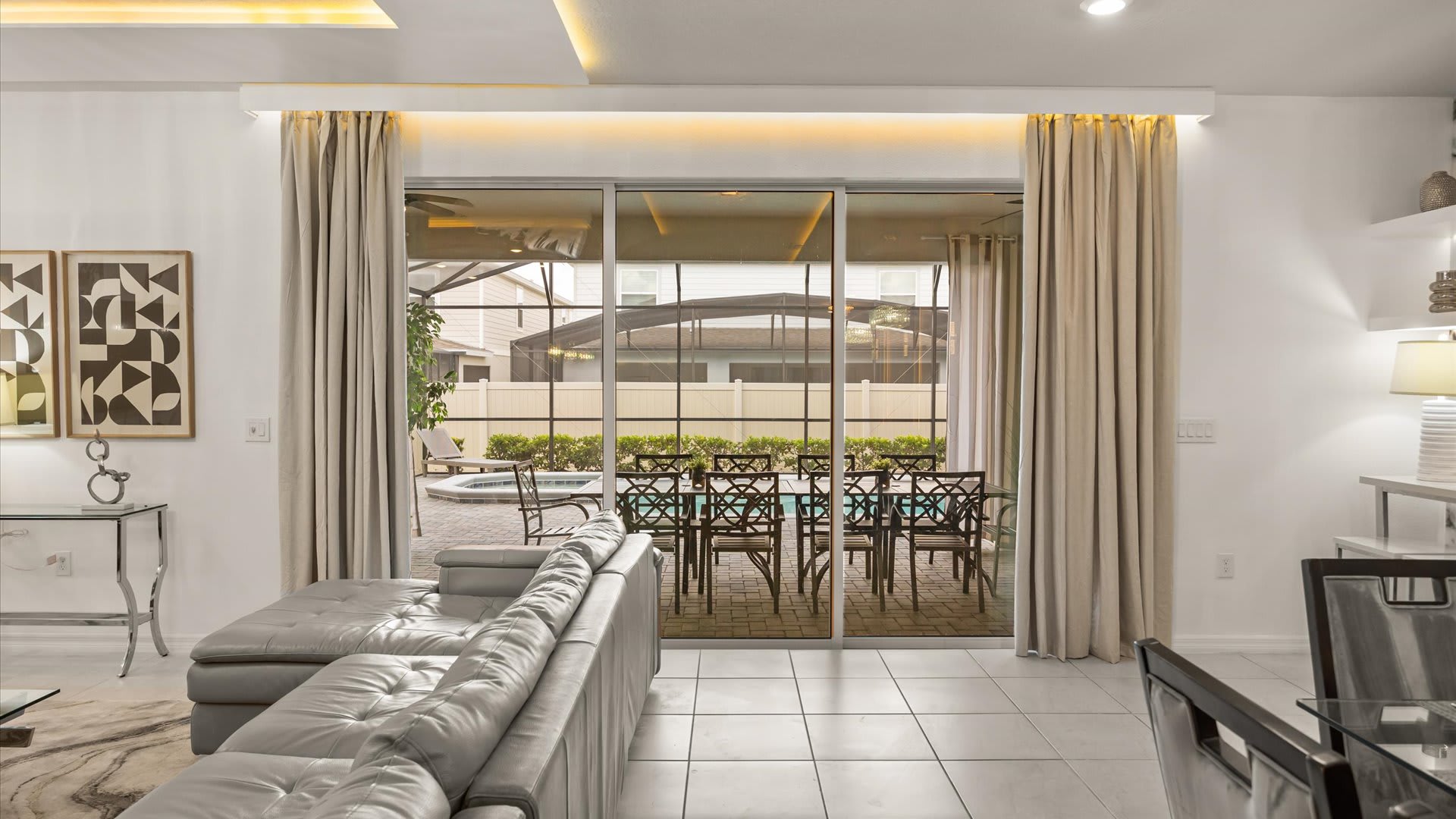 View from the living room through wide sliding glass doors to a screened-in patio with an outdoor dining set and a glimpse of a swimming pool.