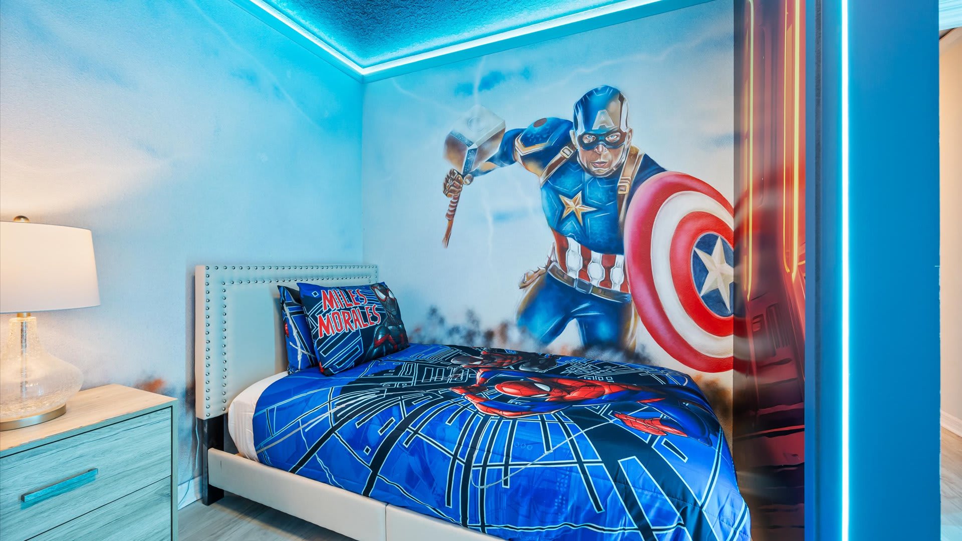 Close-up of the "Spiderman" themed bedroom, featuring a single bed with a Captain America mural on the wall, a modern nightstand, and a lamp.