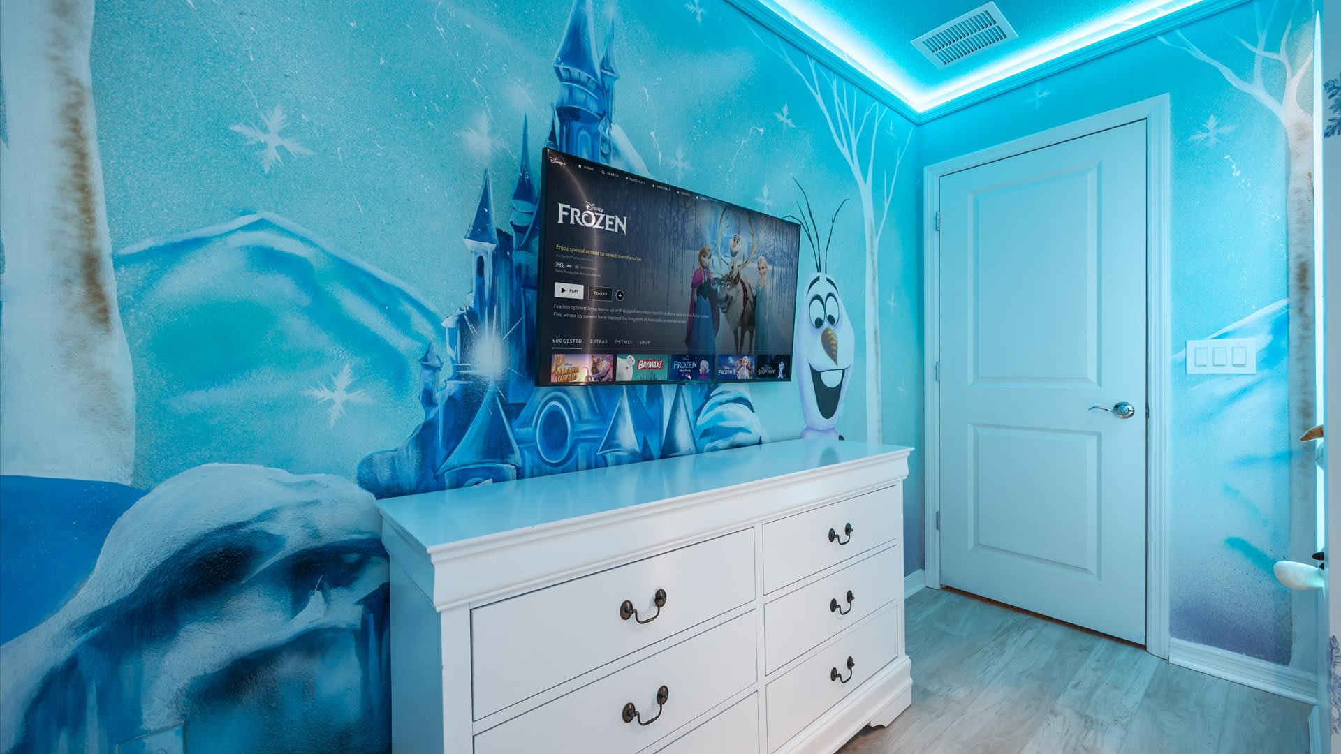Themed children's bedroom featuring a "Frozen" mural on the walls, a white dresser, and a wall-mounted TV displaying the movie, with blue LED strip lighting along the ceiling.