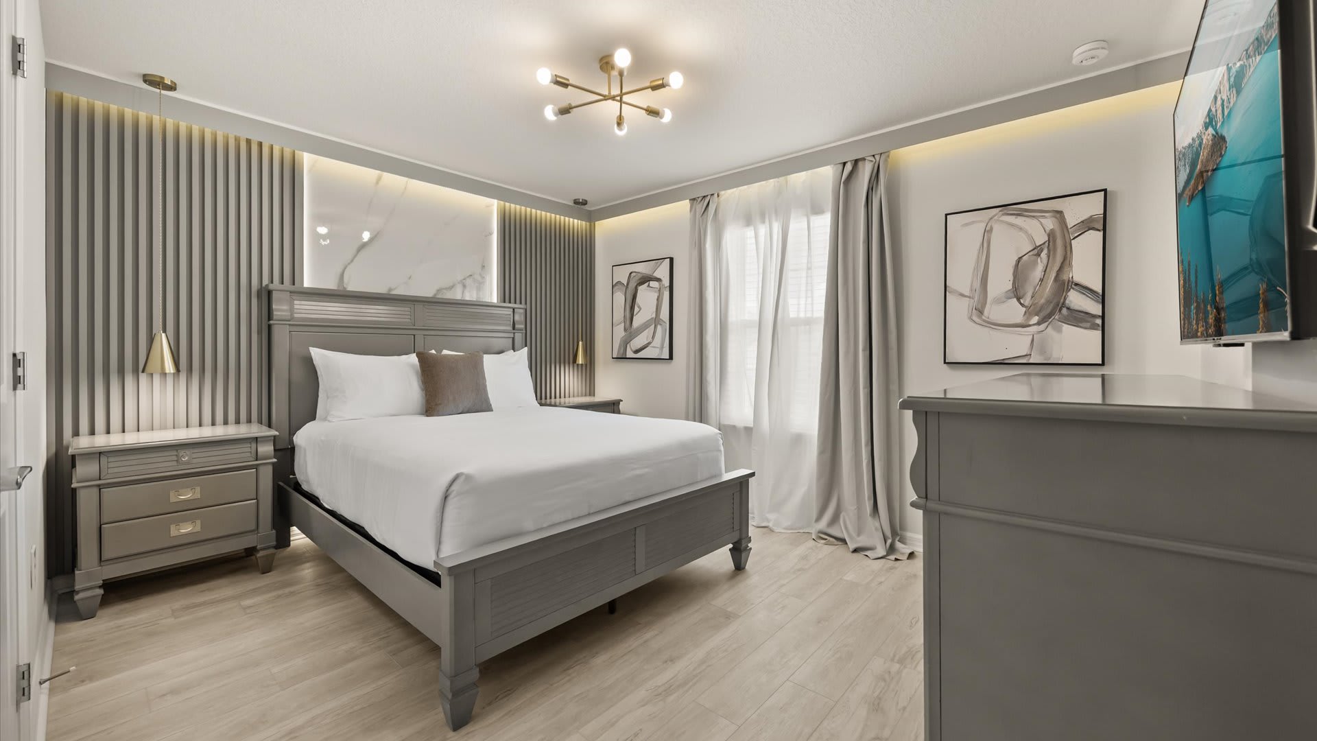 A sophisticated bedroom featuring a grey wooden king bed, light wood flooring, and a grey slatted accent wall with a marble-like panel and integrated lighting.