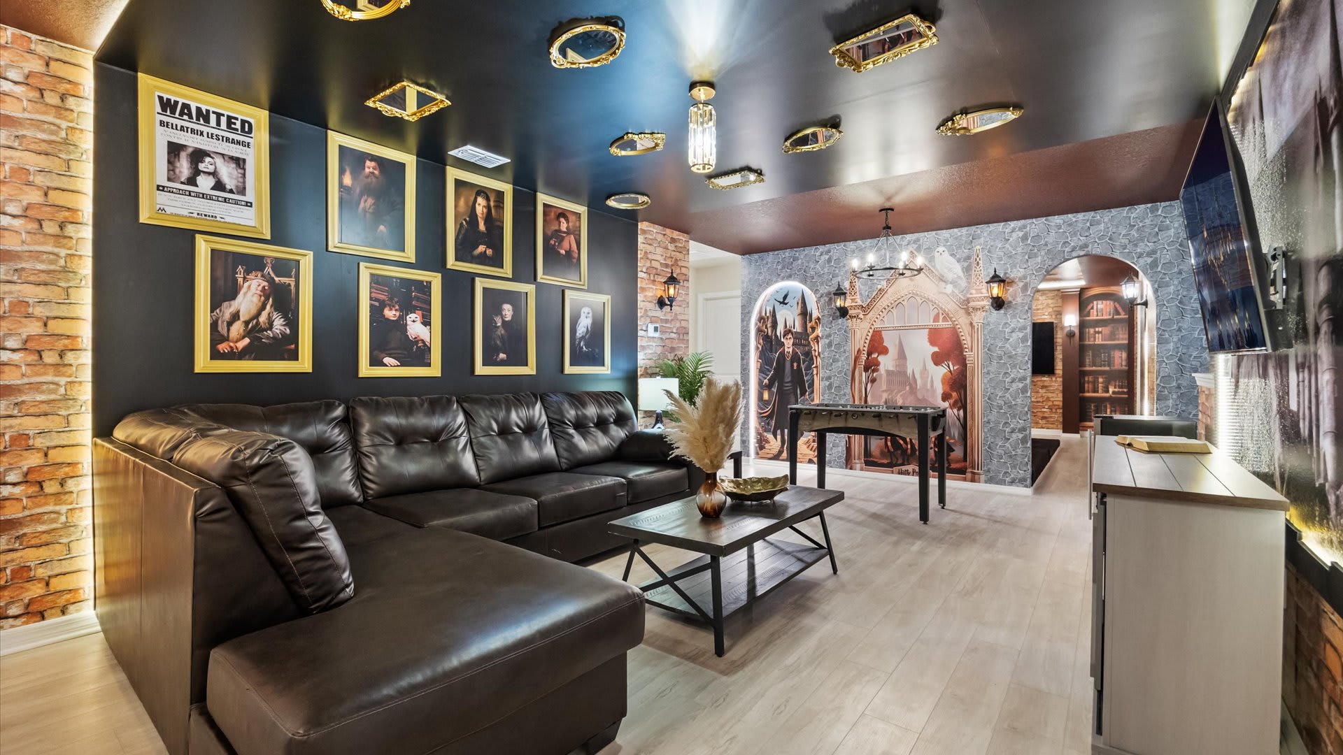 Another perspective of the Harry Potter-themed media room, showing the dark leather sectional, a coffee table, and walls adorned with "Wanted" posters and framed portraits, under a dark ceiling with ornate mirrors.