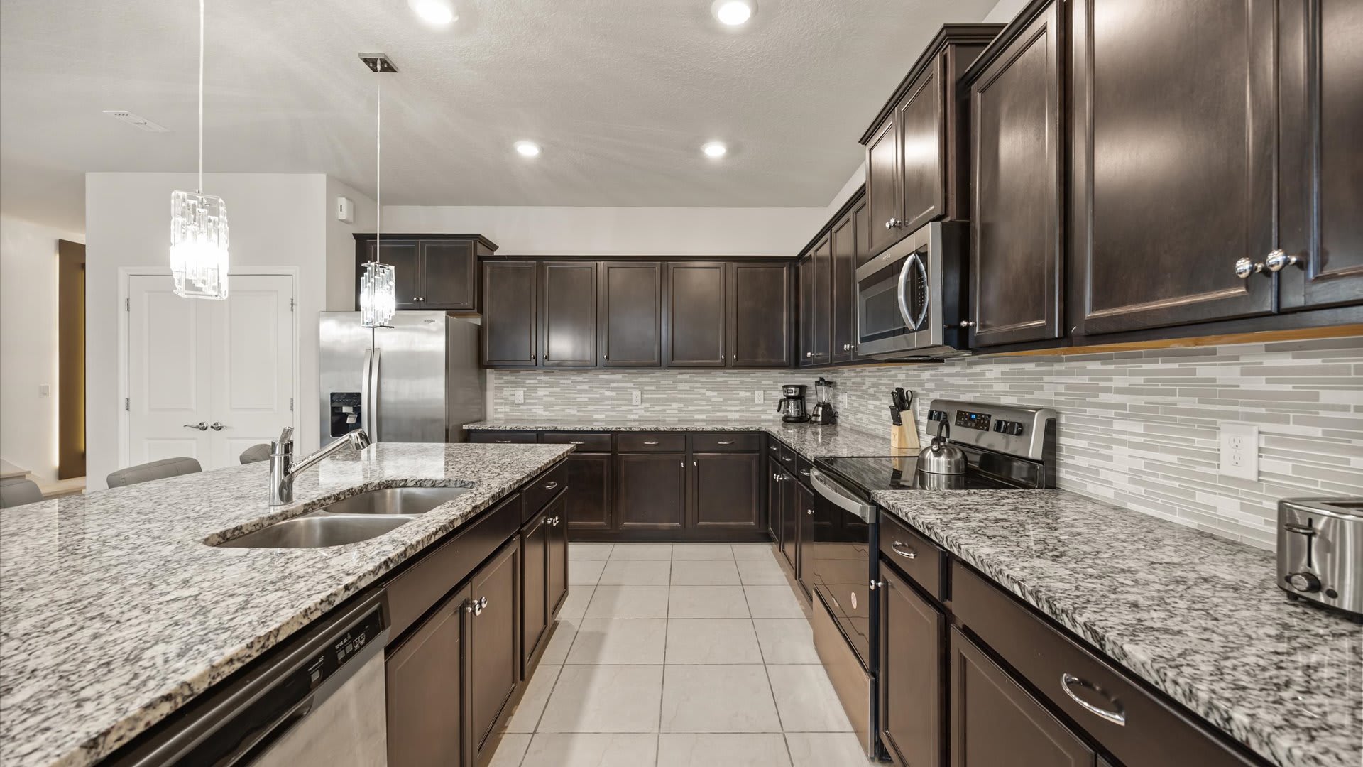 Detailed view of the kitchen showing extensive dark wood cabinetry, granite countertops, a light-colored tile backsplash, and stainless steel appliances including a stove and microwave.