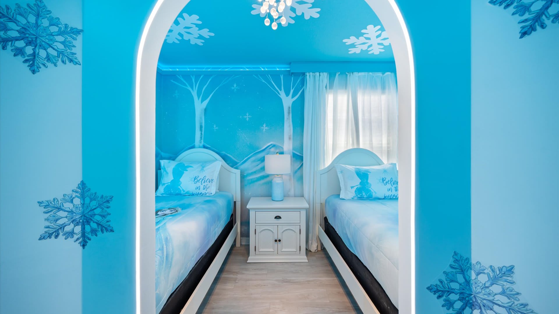 View through an archway into the "Frozen" themed bedroom, revealing two single beds with matching bedding, separated by a white nightstand and lamp.