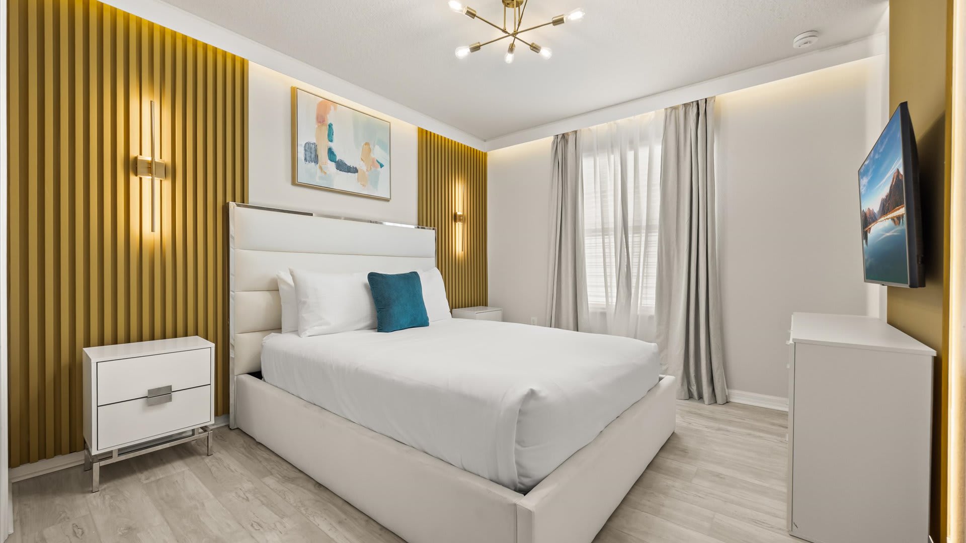 A bright and modern bedroom featuring a white upholstered queen bed, light wood flooring, and a striking gold slatted accent wall with integrated lighting and sconces.