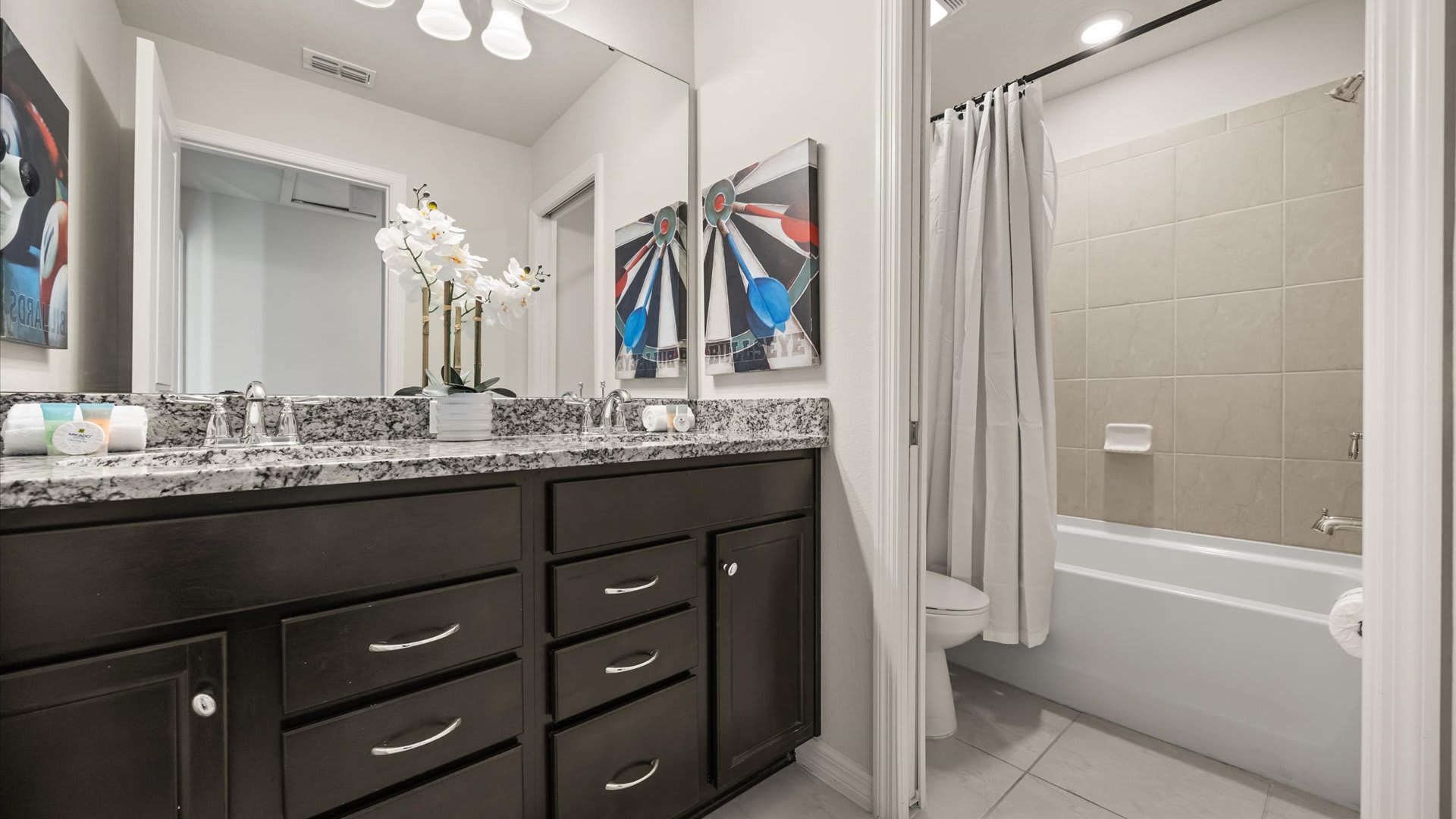 Modern bathroom with a double dark wood vanity, granite countertop, two sinks, and a bathtub with a shower curtain, featuring contemporary artwork on the wall.