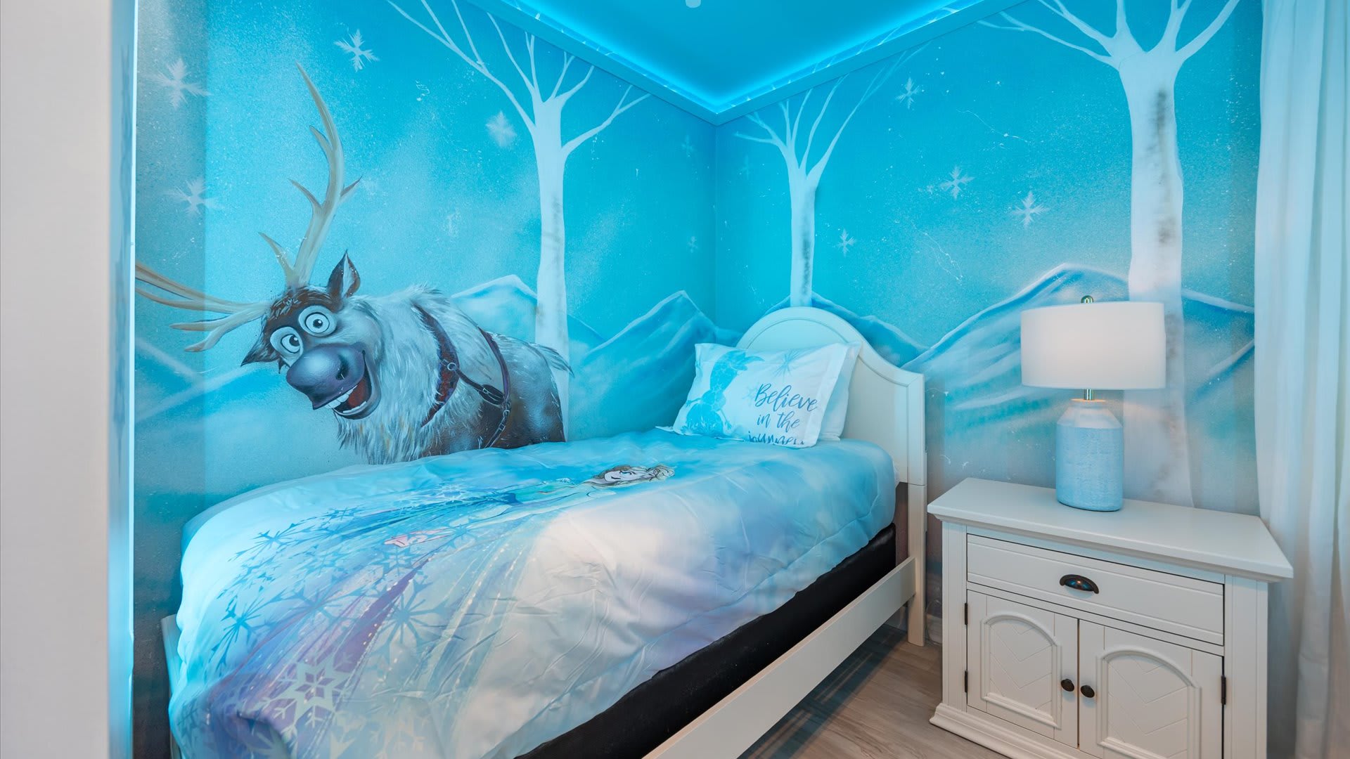 Detailed view of the "Frozen" themed bedroom, showcasing a single bed with a Sven mural on the wall, a white nightstand, and a blue lamp.