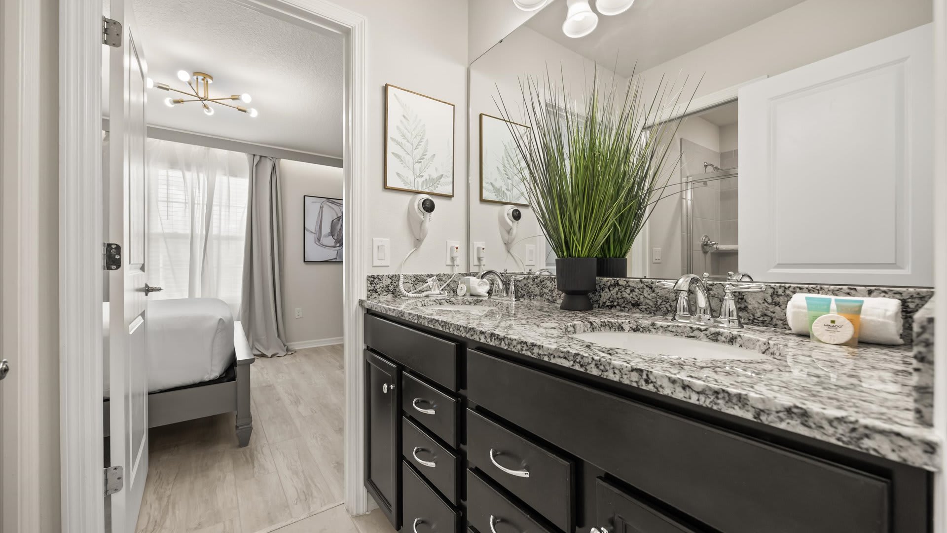 Modern bathroom featuring a double vanity with a speckled granite countertop, dark wood cabinets, and two round sinks, with a view into a light-filled bedroom.